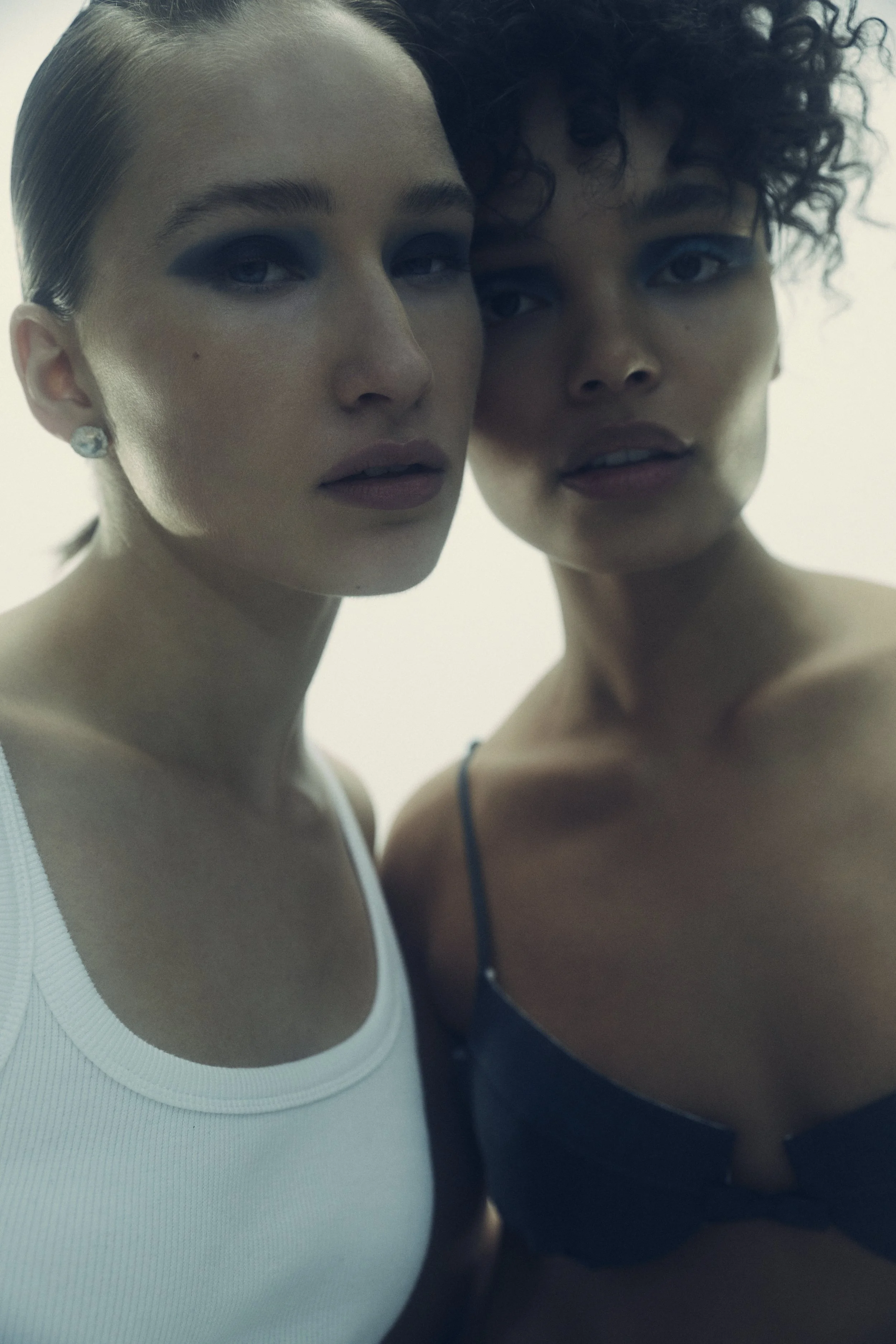 Two women with contrasting hairstyles and makeup, close-up portrait with soft lighting.