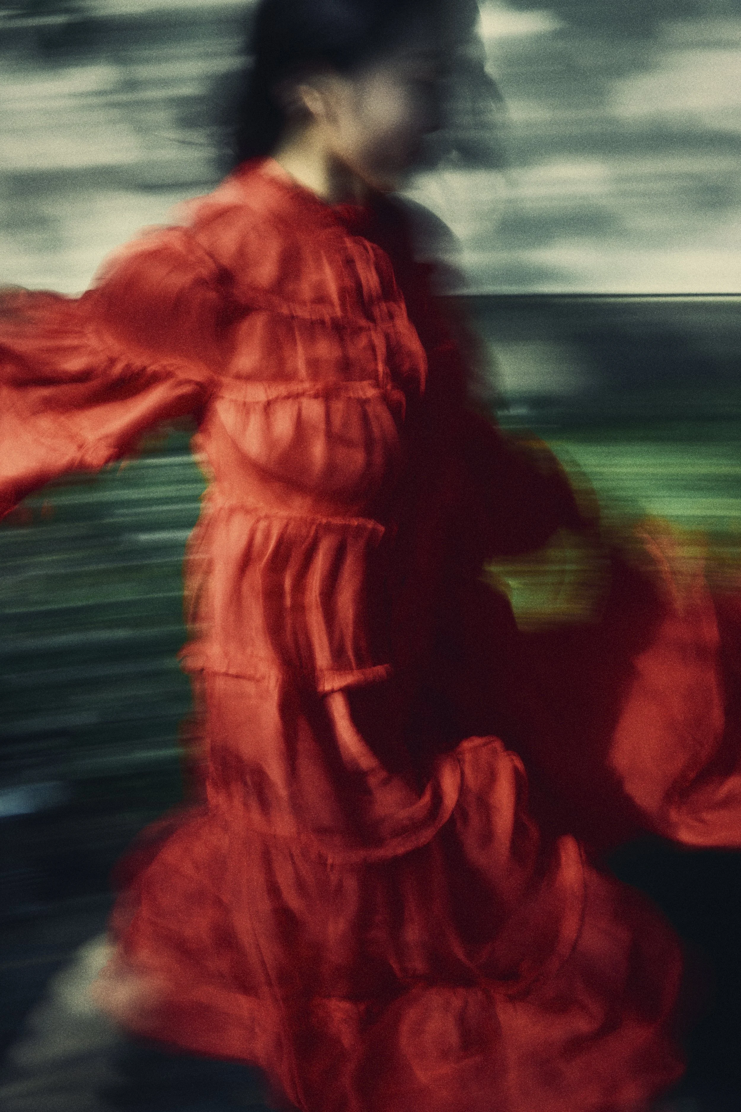 Motion-blurred image of a woman in a red dress running outdoors, with blurred greenery in the background.
