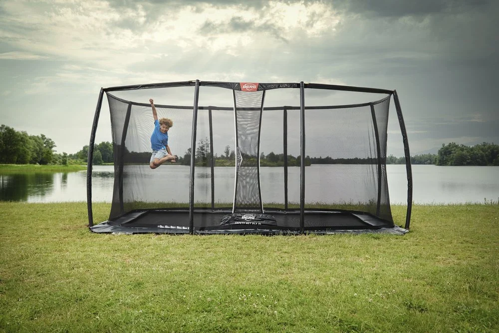 Ein Junge springt in einen Basketballkorb, der im Freien auf einer Wiese neben einem See steht.
