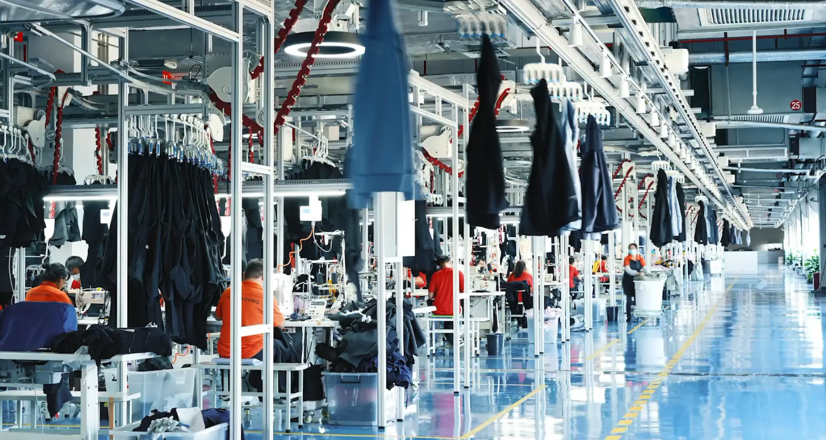 Manufacturing factory with workers sewing dark-colored clothing at workstations.