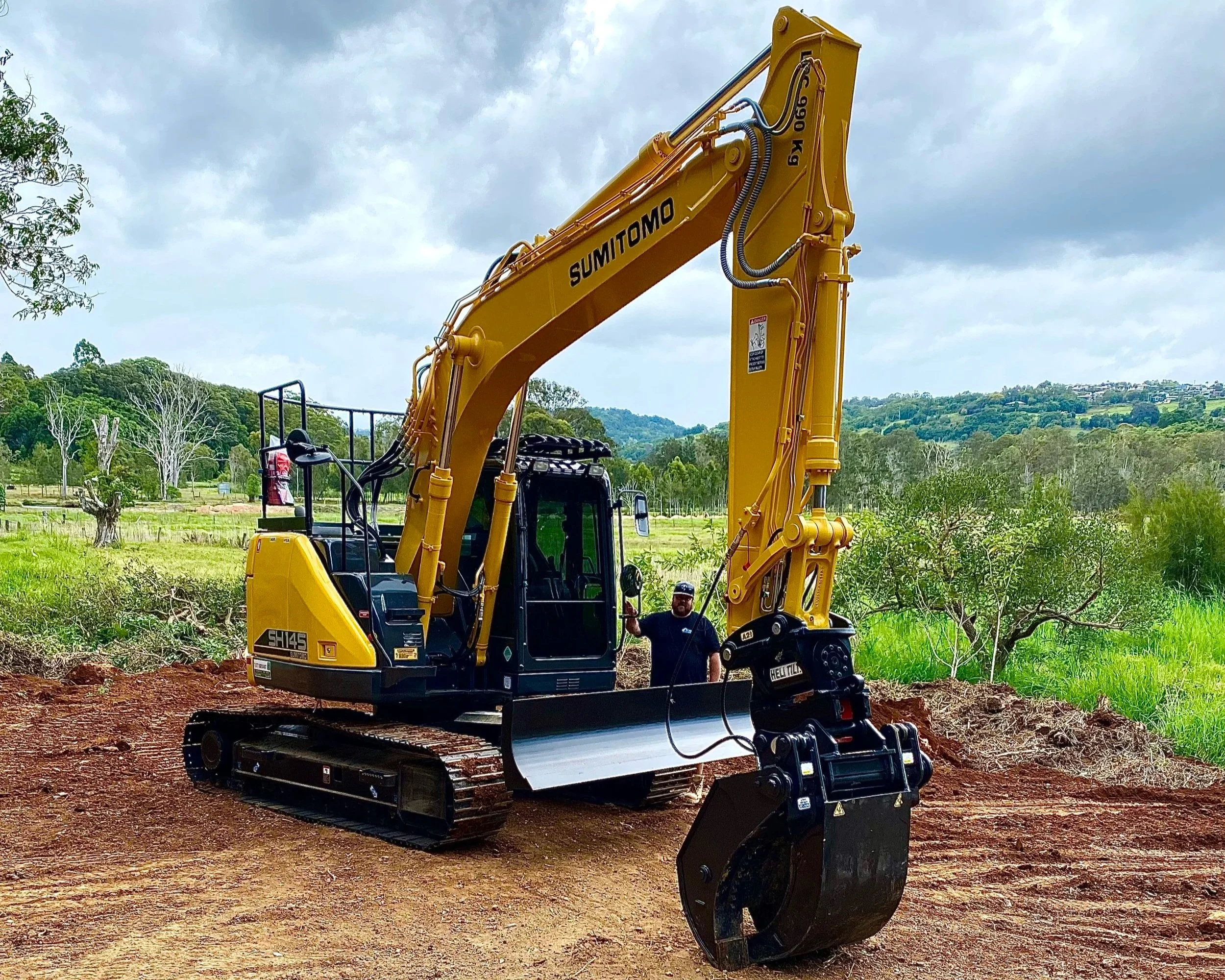 Man standing in front of 14 tonne Sumitomo excavator on earthmoving site in Northern NSW