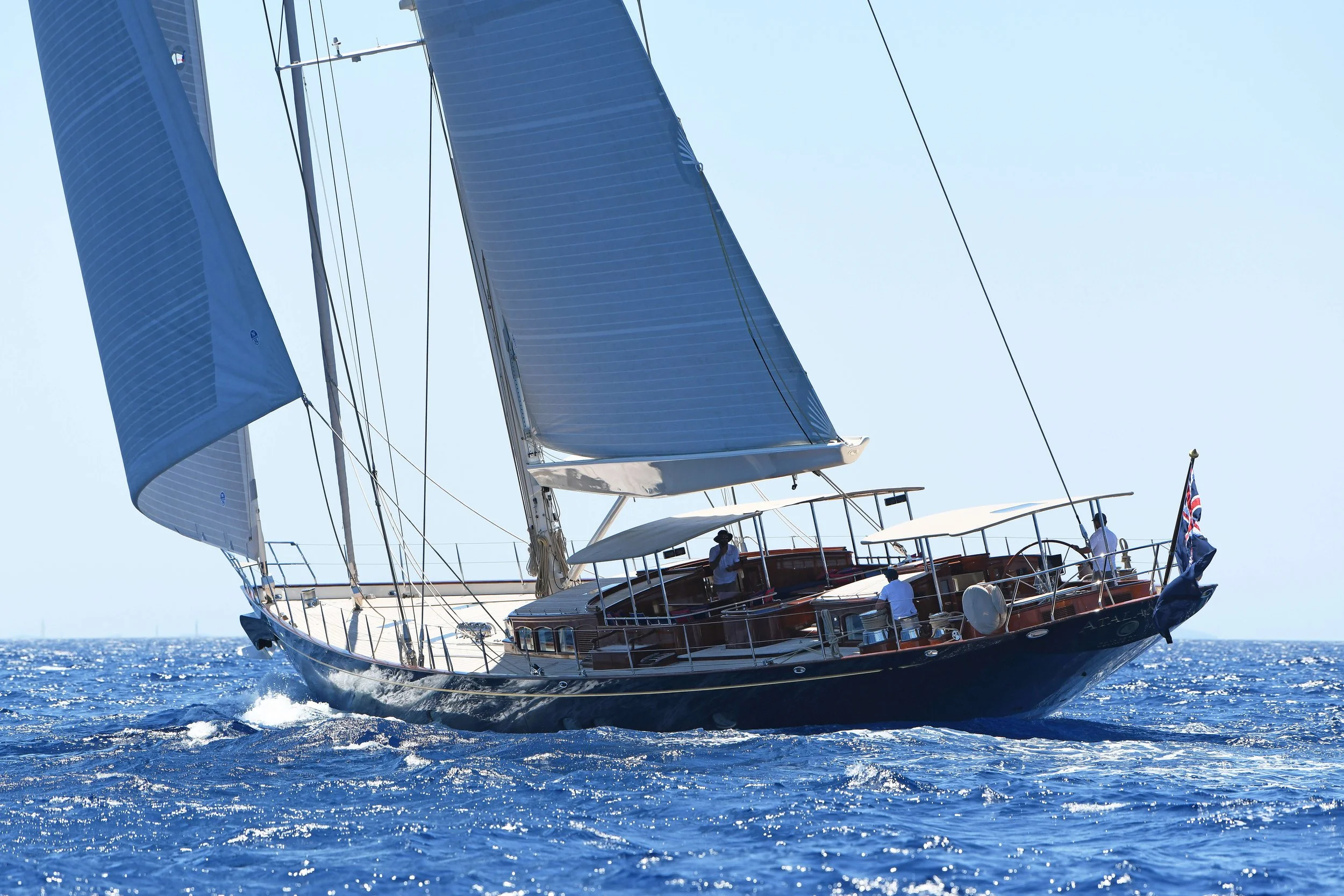 A luxury yacht sailing on the ocean with blue sails and a crew on deck.