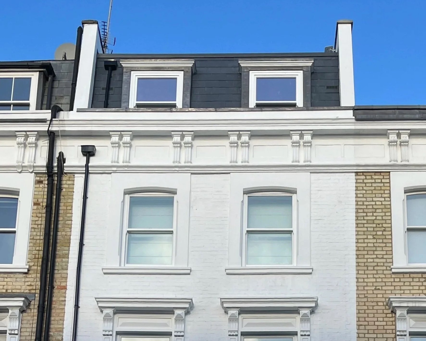 A multi-story building with Victorian-style architecture, painted white, with decorative moldings and large windows, with a mansard roof and blue sky in the background.
