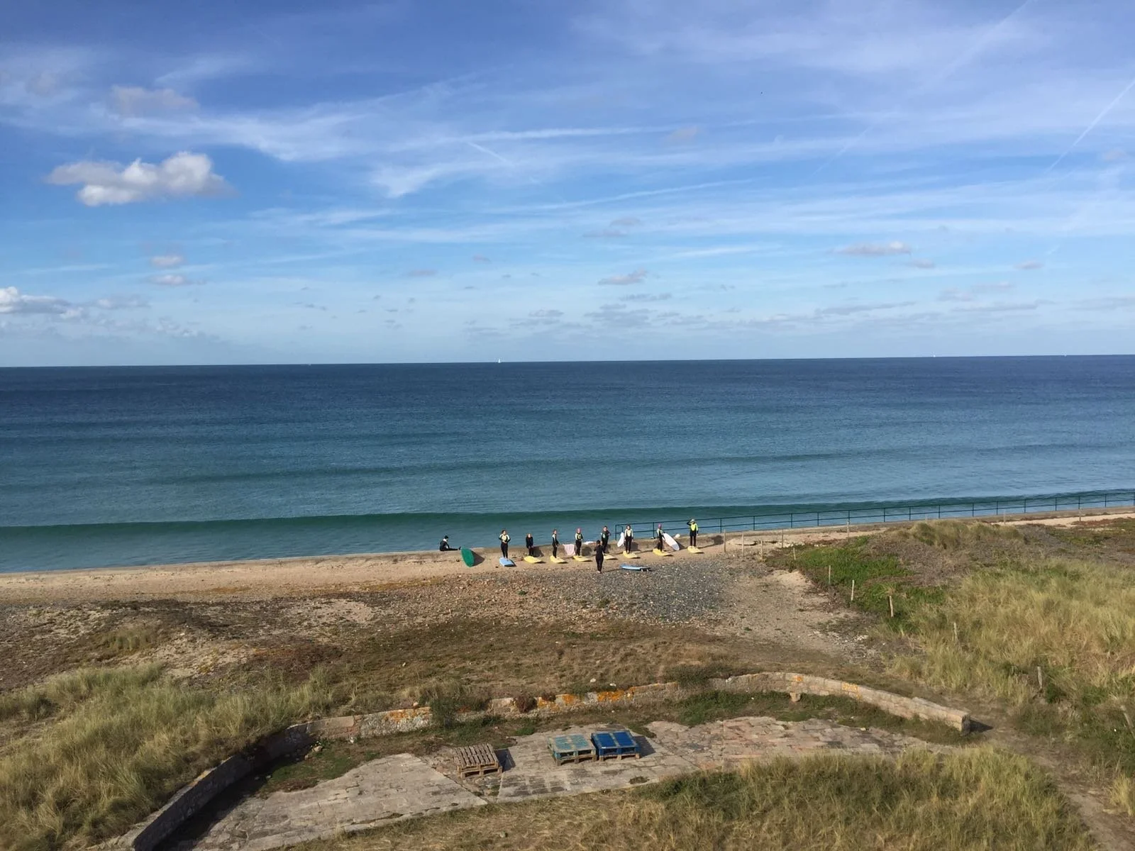 People walking along the beach carrying surfboards, with the ocean and blue sky in the background.