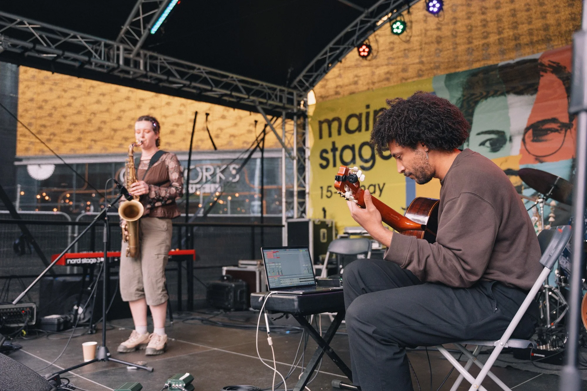 woman playing saxophone and man playing classical guitar on stage at a jazz festival