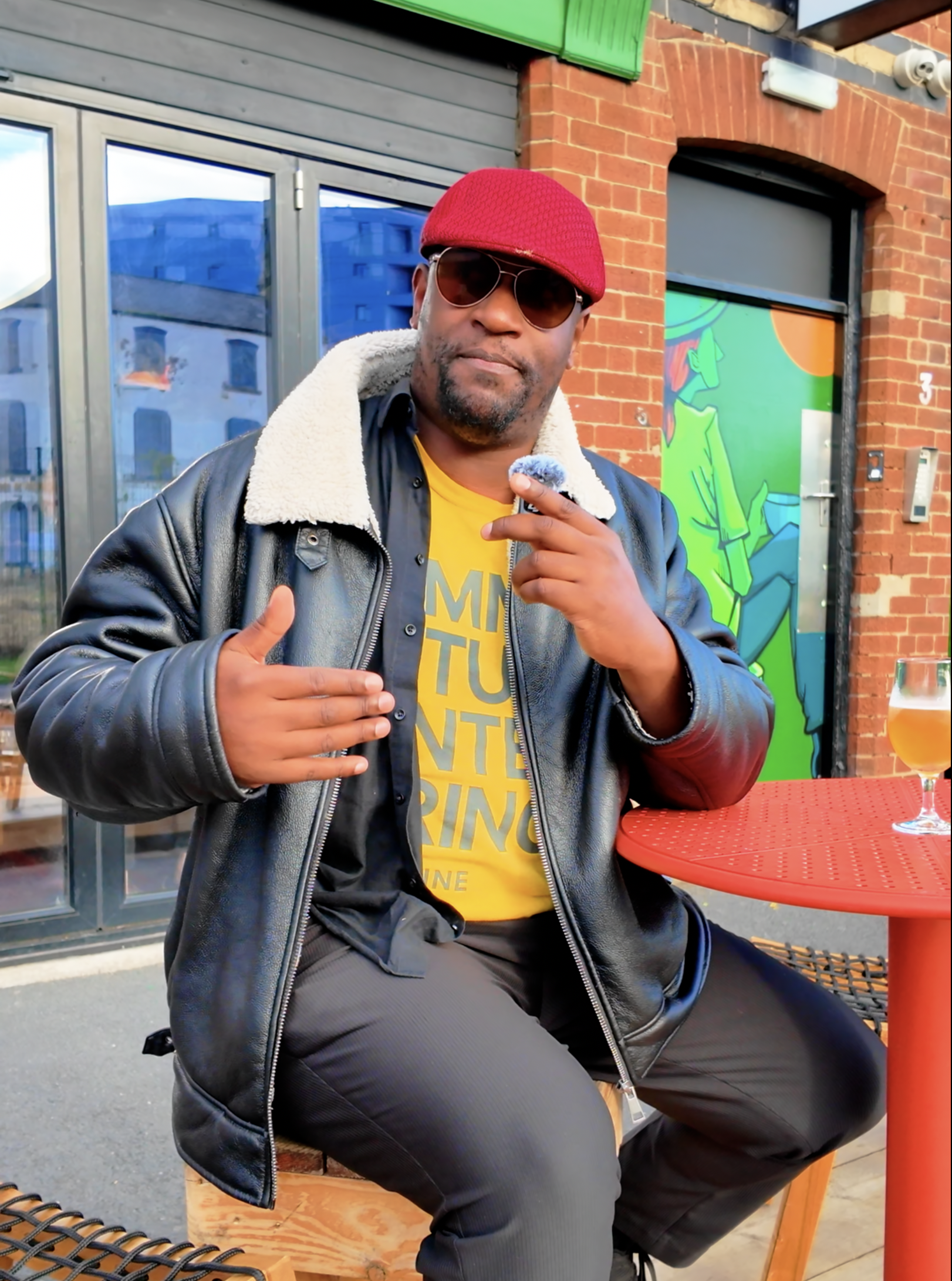 man on stool wearing red hat outside of a music venue.