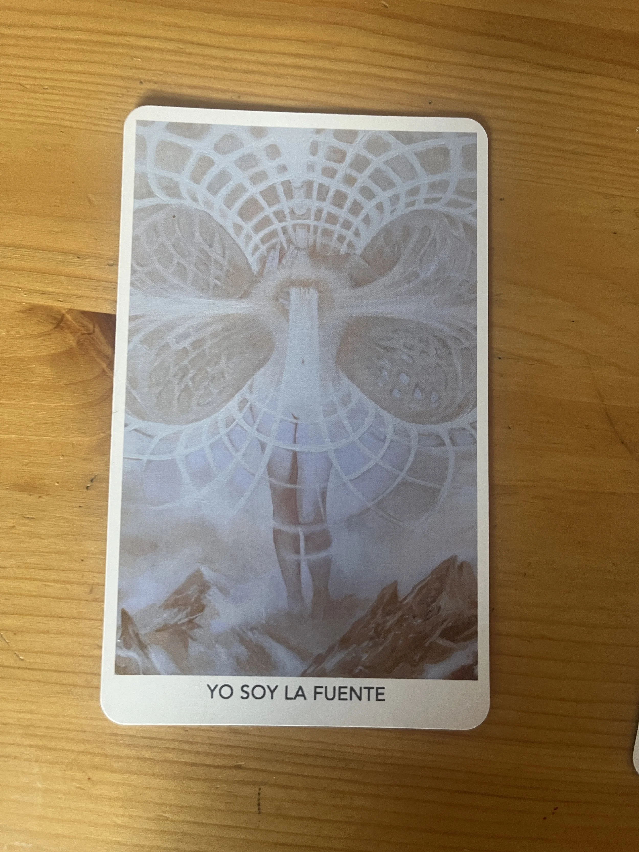 A tarot card featuring a large butterfly with intricate wing patterns and a central body that extends downward, standing on mountain peaks, with a geometric halo above it. The card has the Spanish words "YO SOY LA FUENTE" at the bottom.
