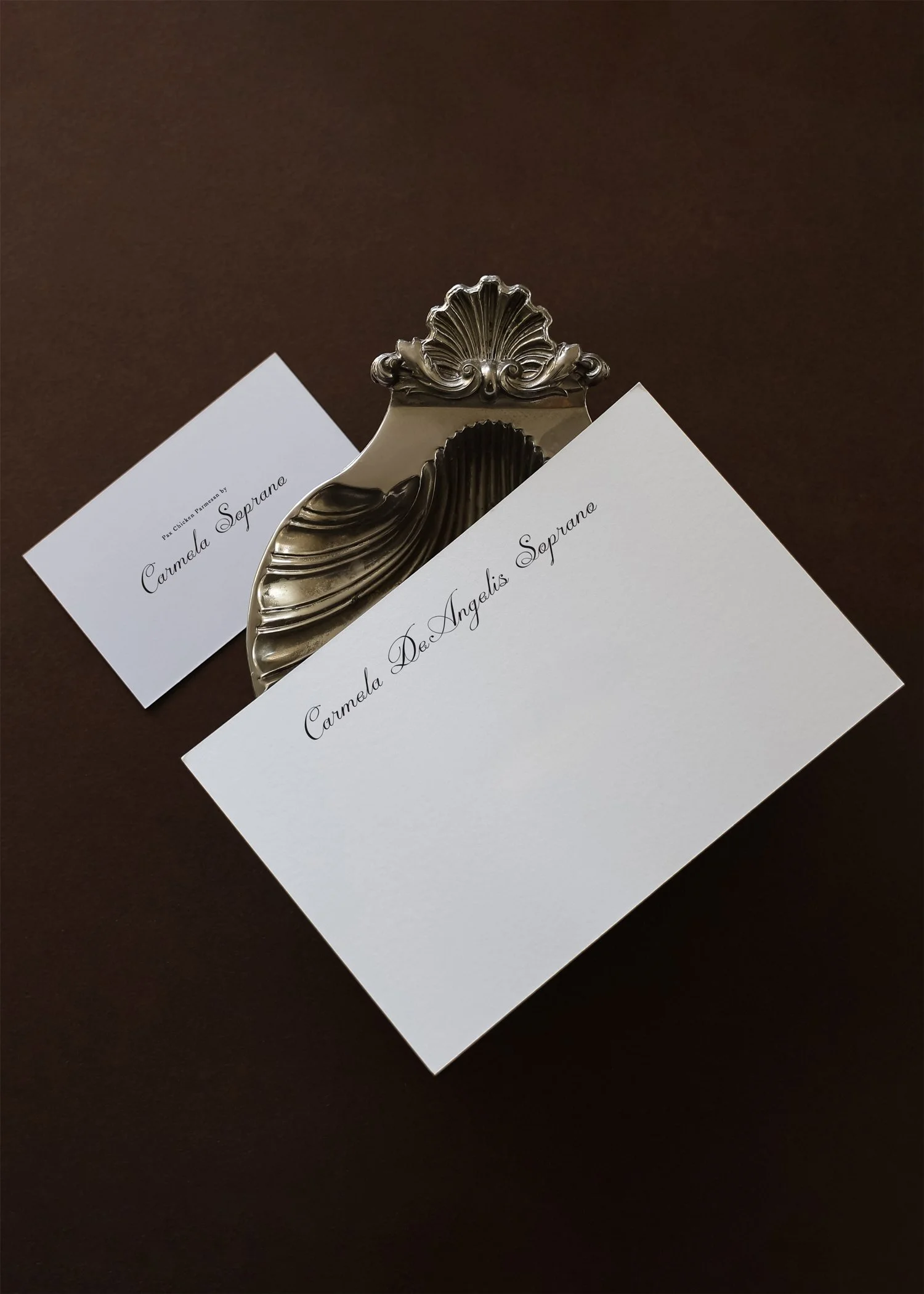 Drie witte RSVP-kaarten met zwart cursief lettertype, één grote kaart in het midden en twee kleinere kaarten ernaast, geplaatst in een sierlijke zilveren papierhouder op een bruine achtergrond.