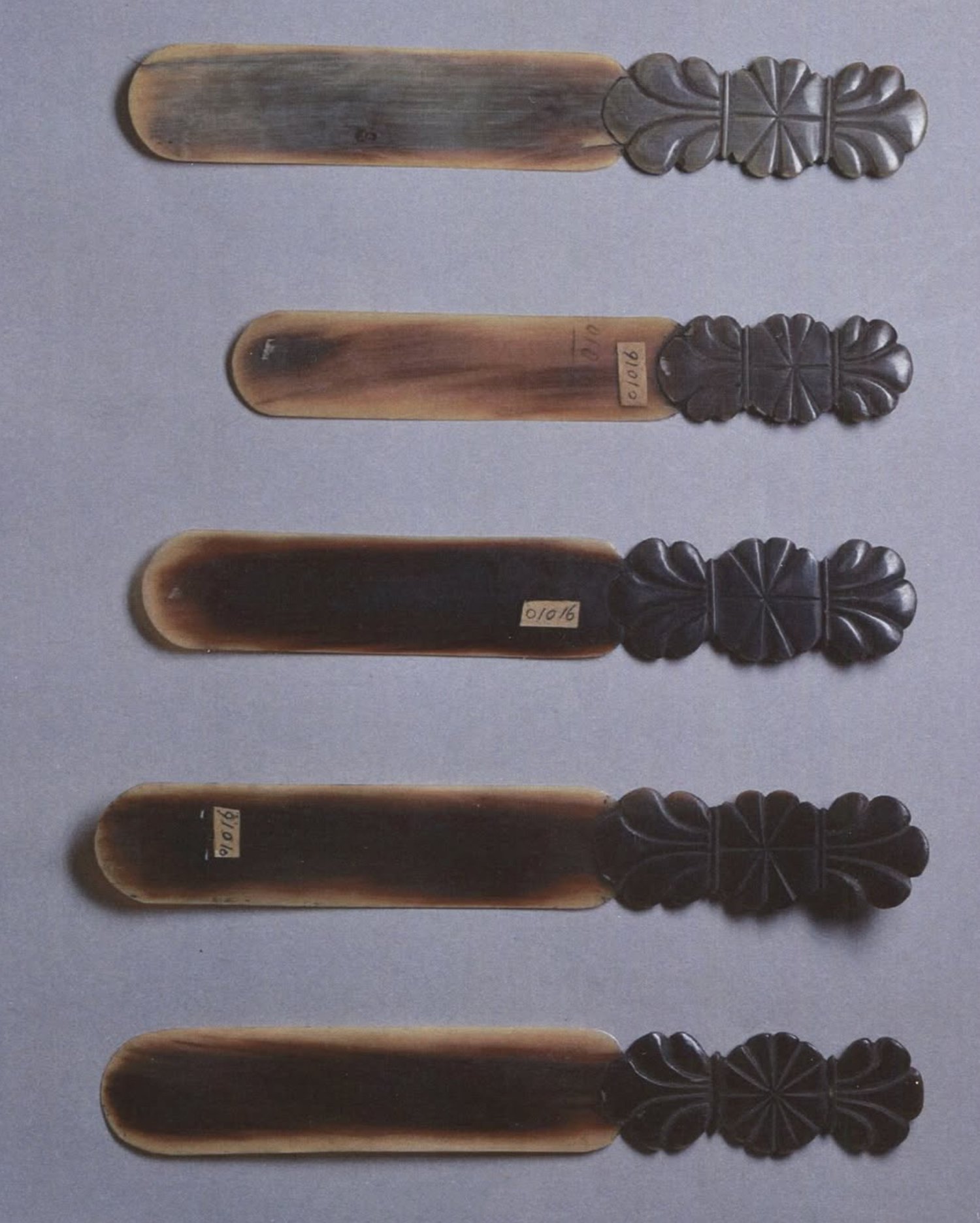 Vier oude houten en metaal gereedschappen of decoratieve voorwerpen met geverfde zwarte details, liggend op een lichte achtergrond.