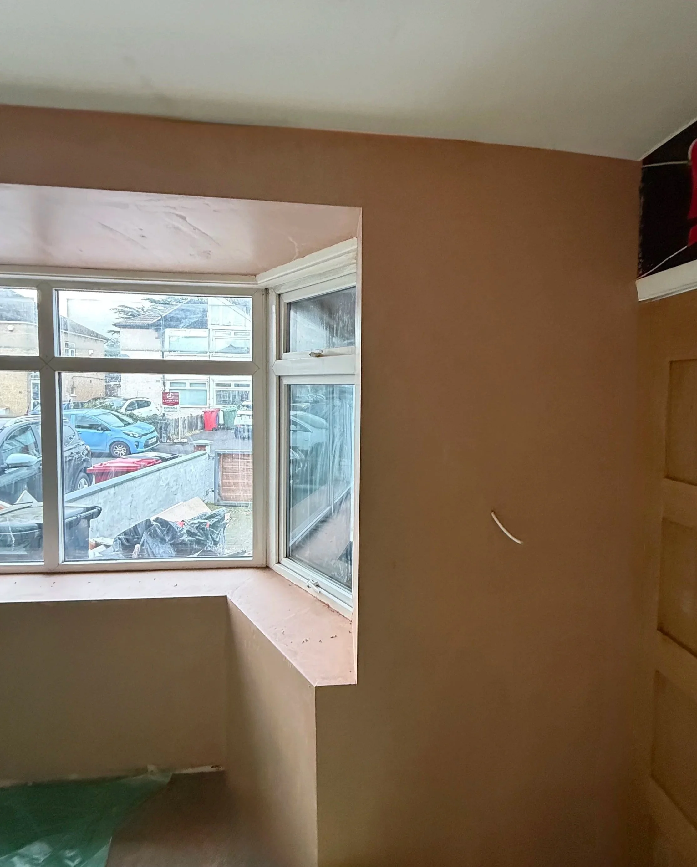 View from inside a room looking out a bay window at parked cars on a street.