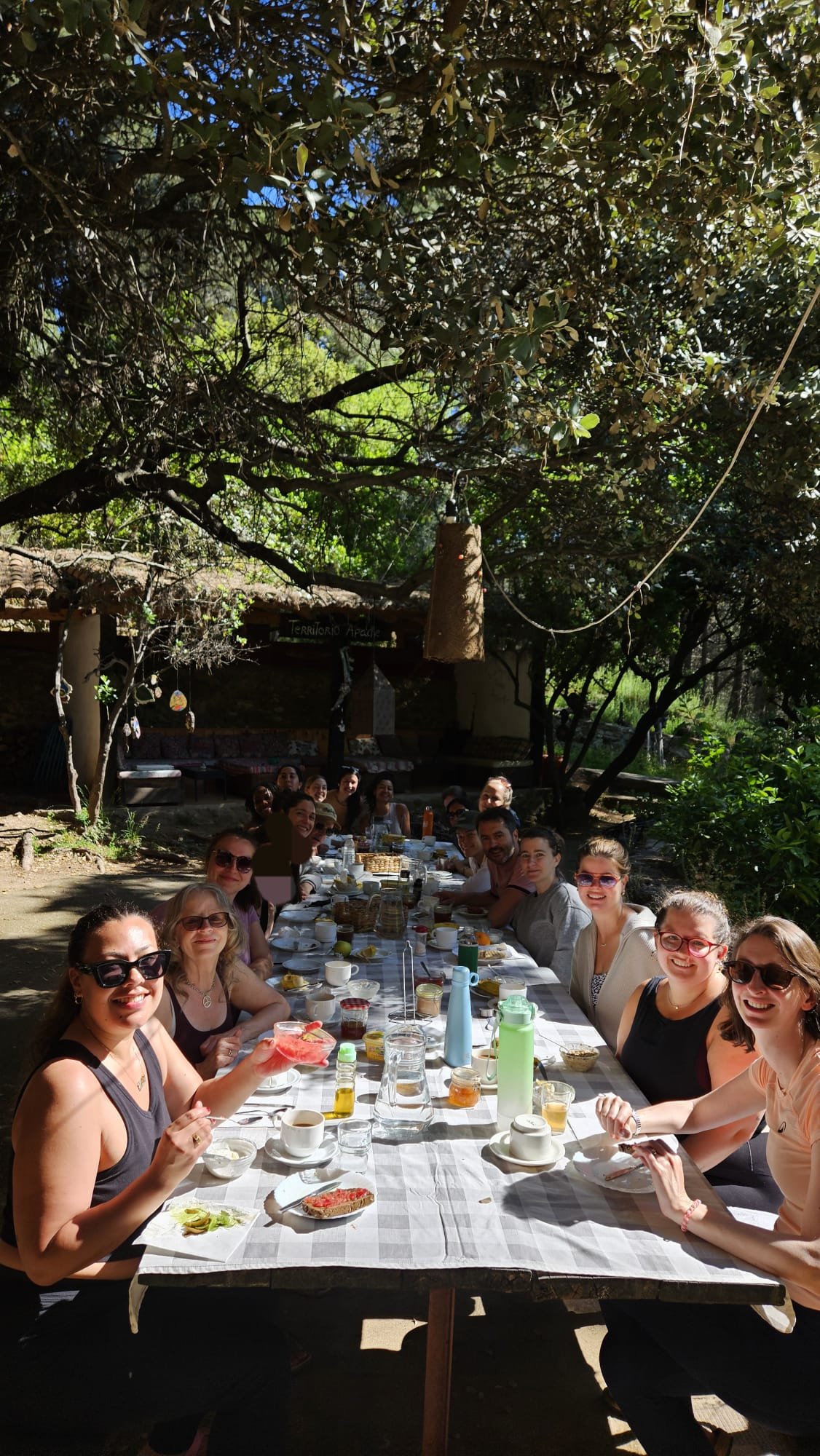 Group photo at breakfast along a long table outside under trees with people smiling