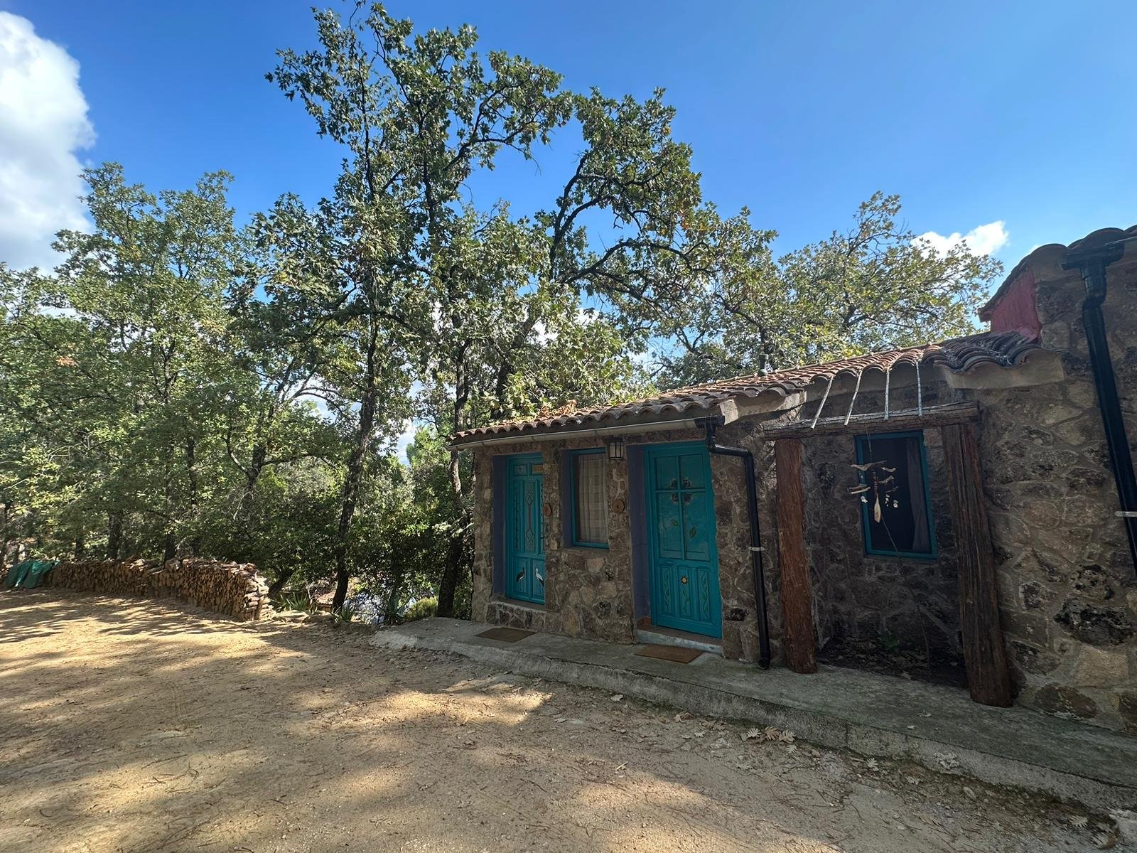 Stone cottage with blue doors and windows, surrounded by trees under a clear blue sky.