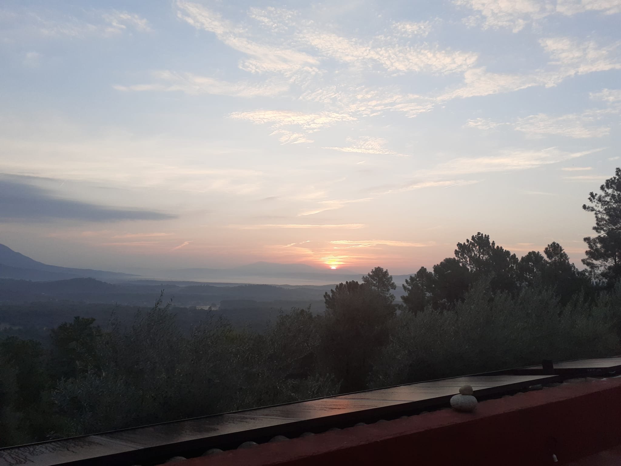 Sunset over a hilly landscape with trees and a few clouds in the sky.