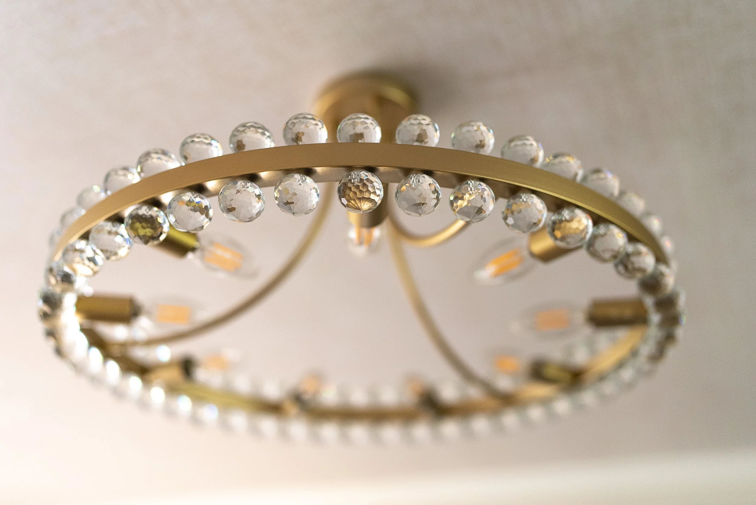 Close-up view of a decorative ceiling light fixture with a gold-colored structure and clear crystal-like beads arranged in a circular pattern.