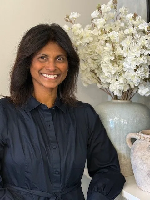 Portrait of Dee Lofgren wearing a black blouse, with white flowers and light-colored vases in the background.