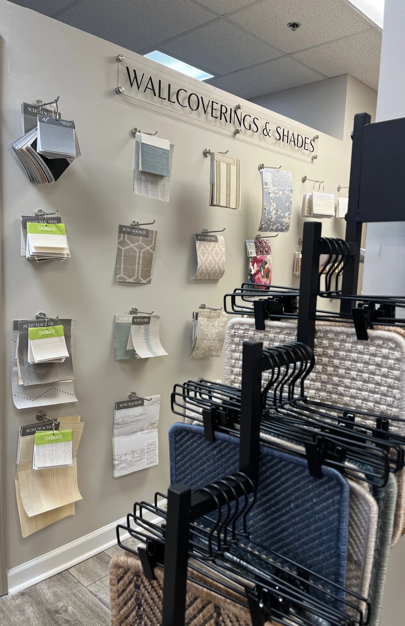 Display of wallpaper samples and fabric swatches in a store, with a sign reading 'Wallcoverings & Shades' at the top.