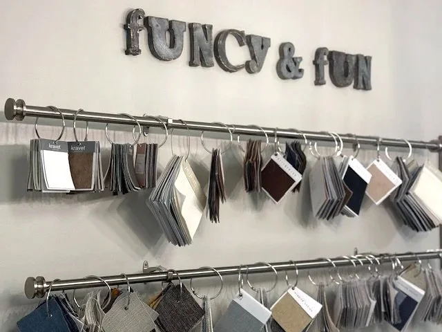 Display of fabric swatches hung on metal rods with a sign above reading 'FUNNY & fun' in decorative letters.
