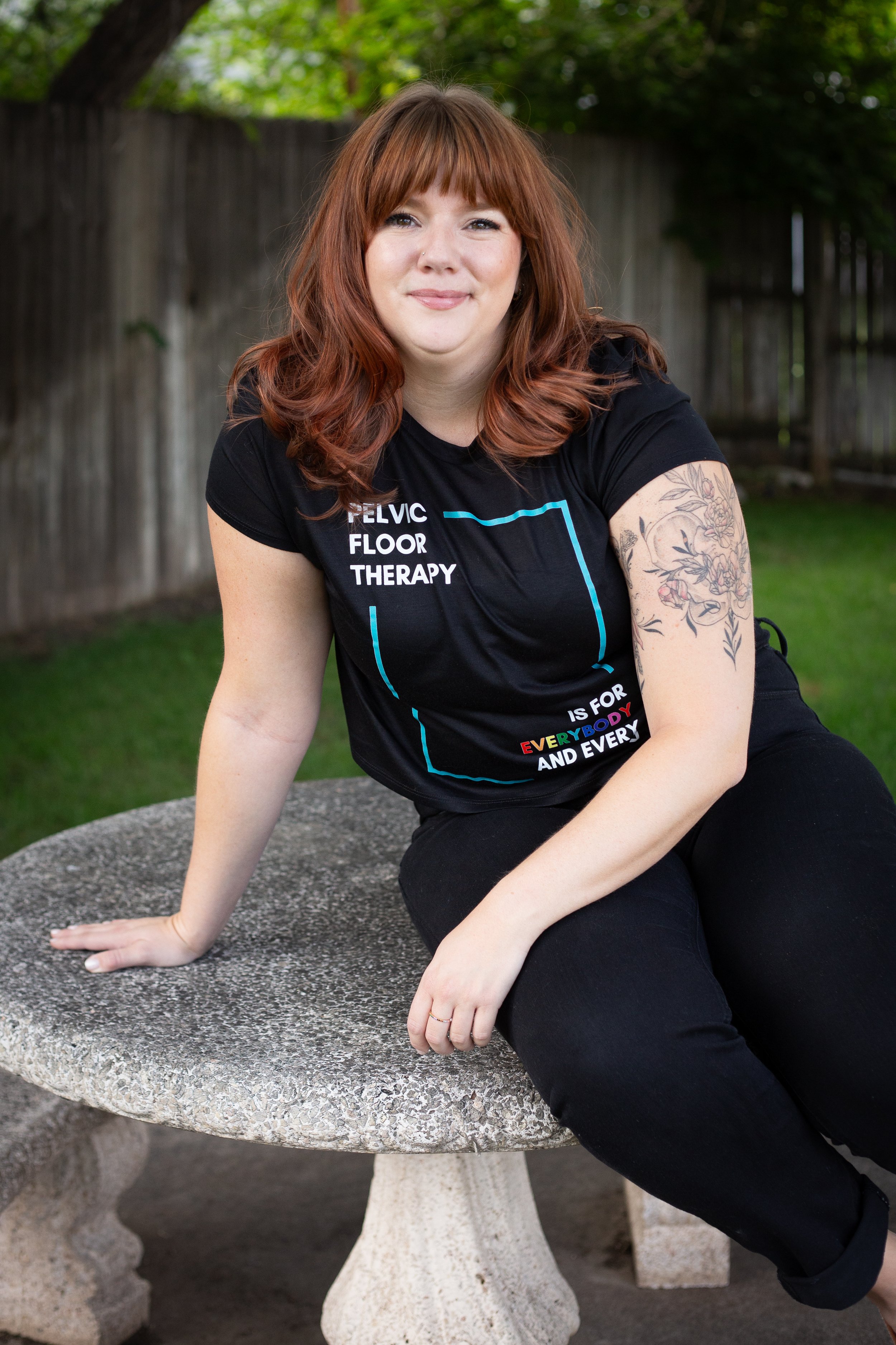 Krystyna headshot outside while wearing a black shirt that says pelvic floor therapy is for everybody and every body