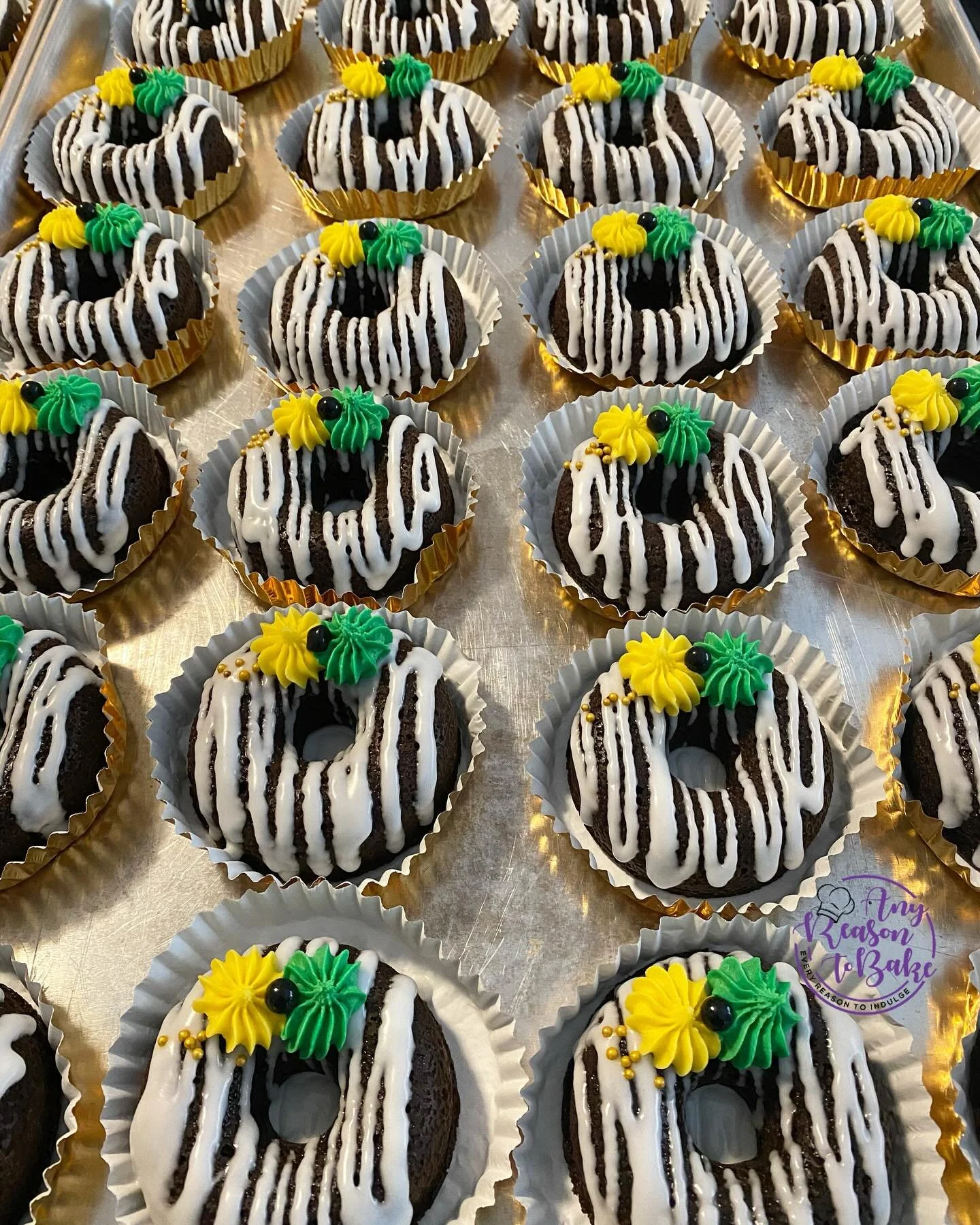 Chocolate donuts decorated with white and black icing, topped with yellow and green frosting flowers and small black and gold beads, arranged on a metallic tray. | Any Reason To Bake