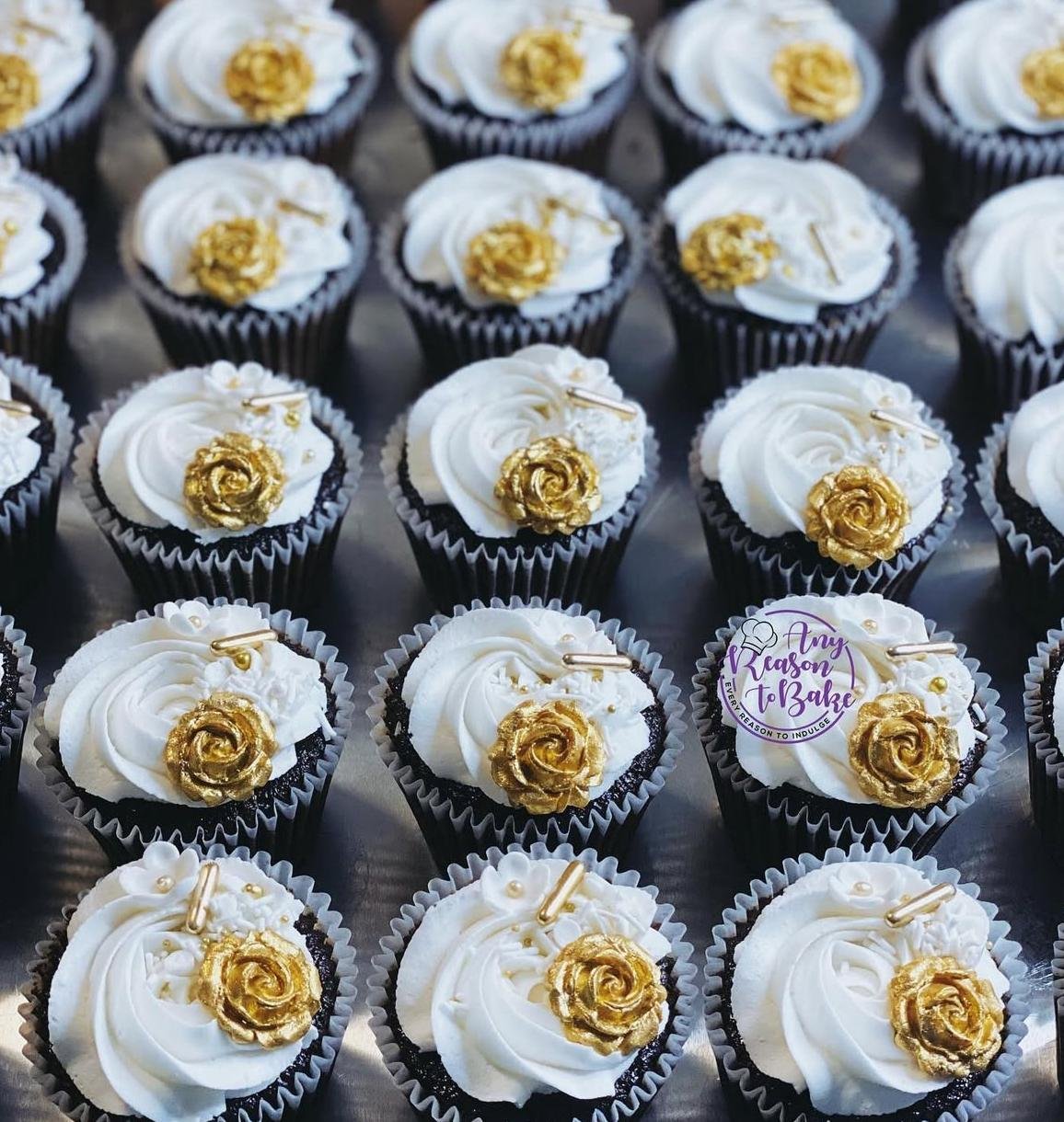 Cupcakes with white frosting, gold rose decorations, and small gold accents, arranged in black and white cupcake liners.