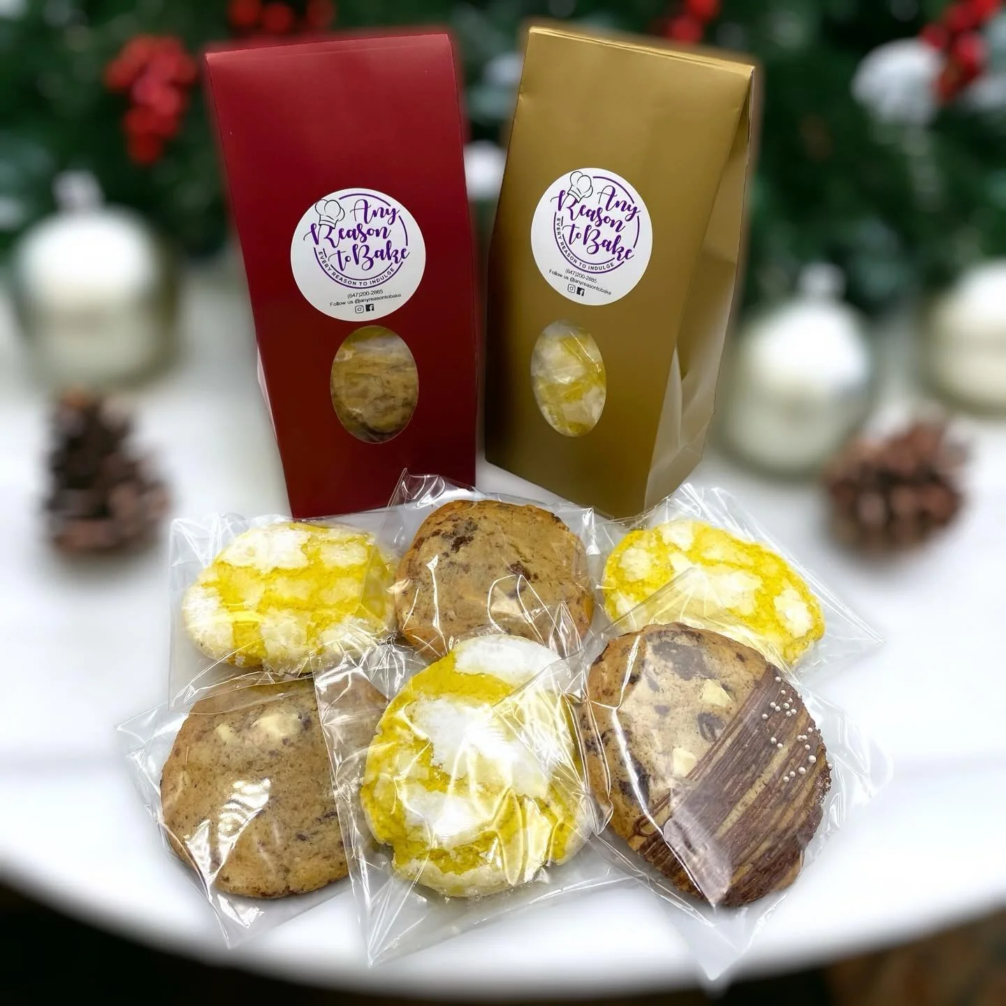 Assorted cookies wrapped in clear plastic on a white surface, with holiday-themed background. Two standing boxes labeled 'Any Reason To Bake' in red and gold.
