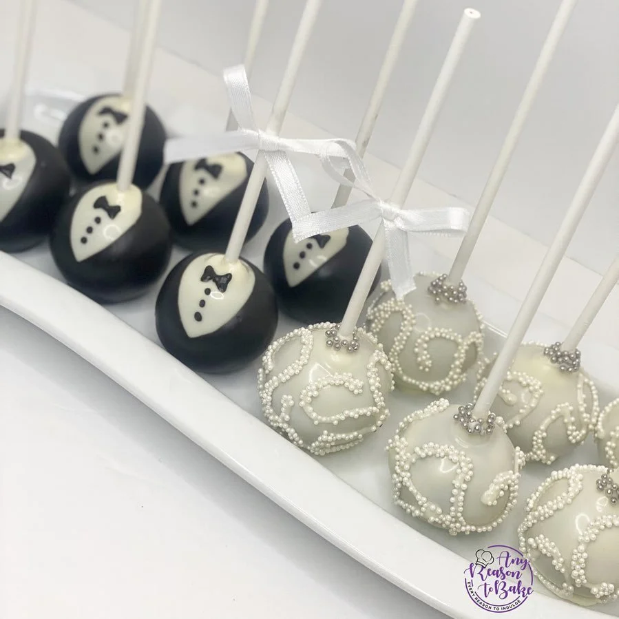 Cake pops decorated as tuxedos and wedding dresses with white and black designs, on a white tray.