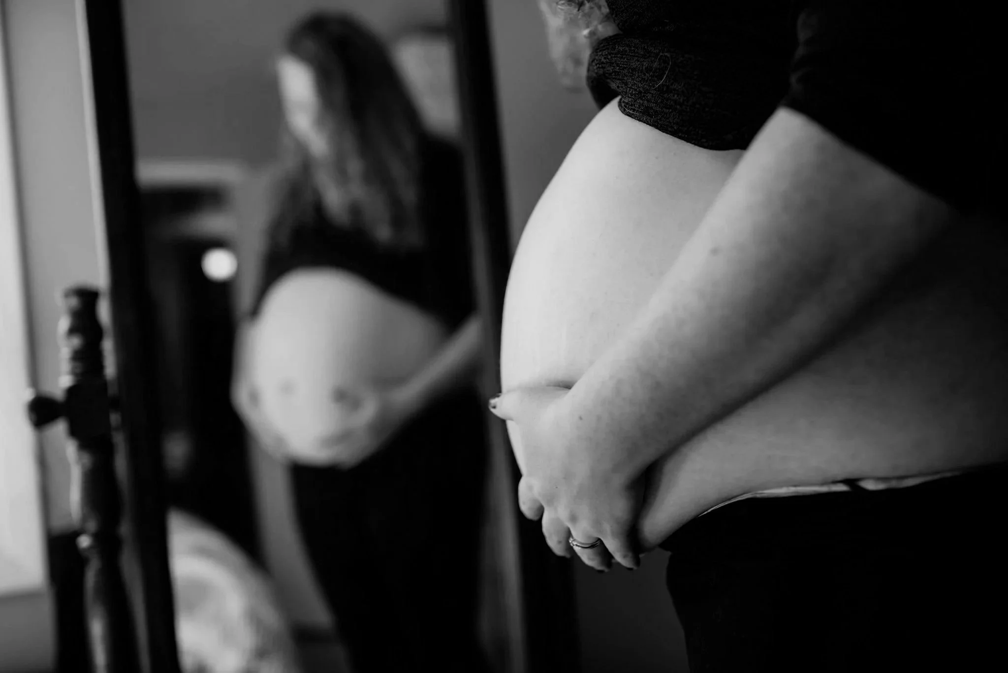 Pregnant woman standing in front of a mirror, holding her belly, with her reflection visible.