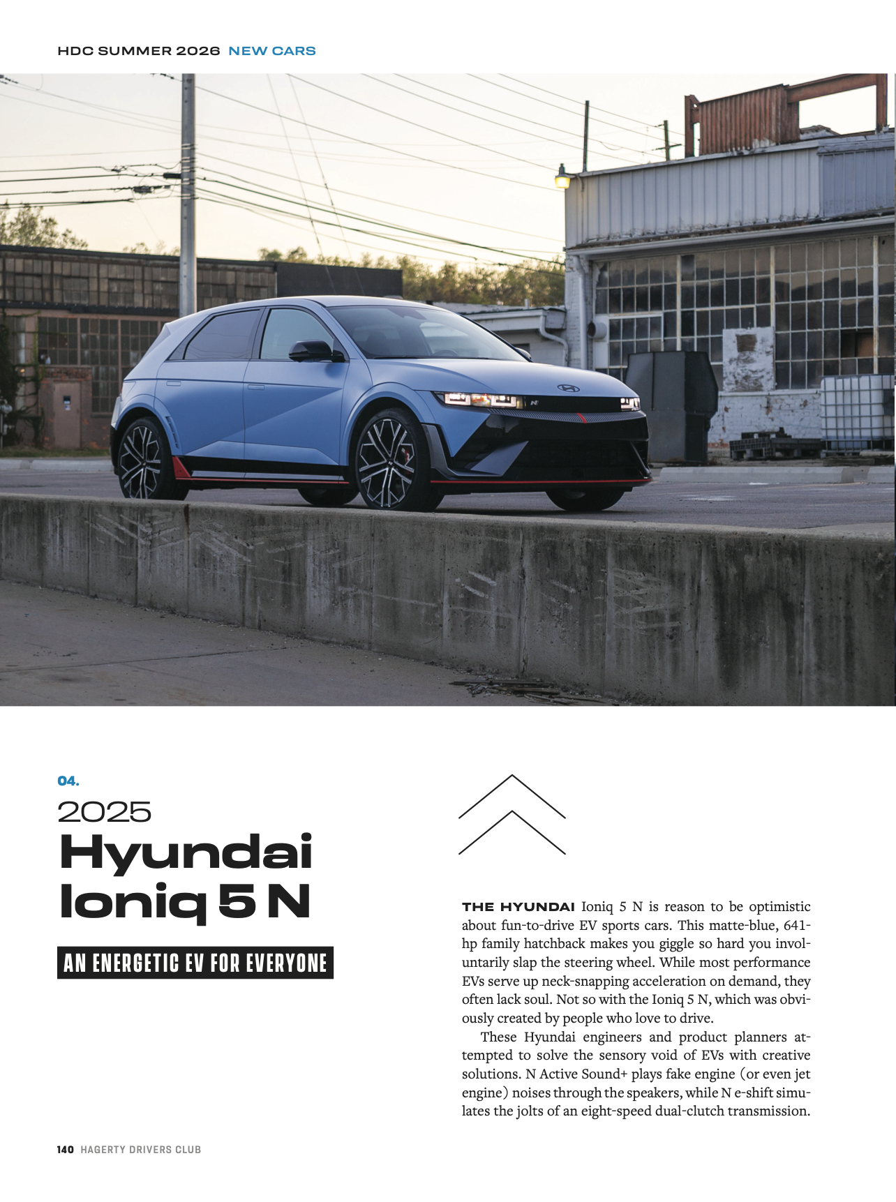 Front view of a matte blue 2025 Hyundai Ioniq 5 N electric sports car parked outdoors near a building with large windows, power lines in the background
