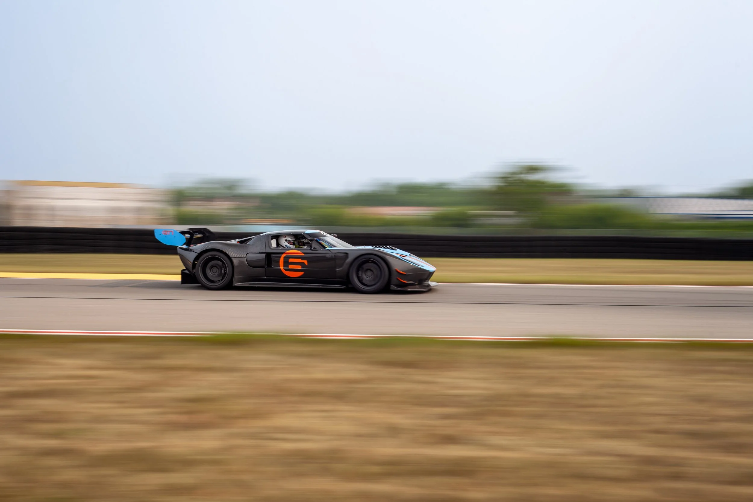 Black race car with orange number 6 racing on a track with motion blur in the background.