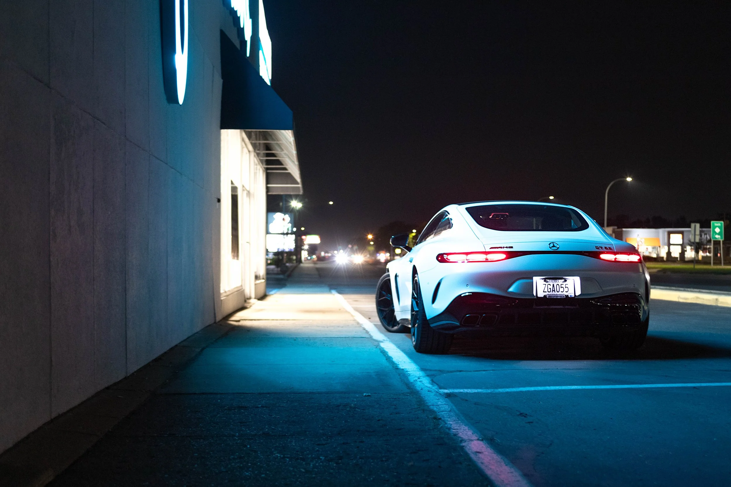 A white Mercedes-Benz AMG GT 63S parked outside a storefront at night, illuminated by streetlights and neon signs.