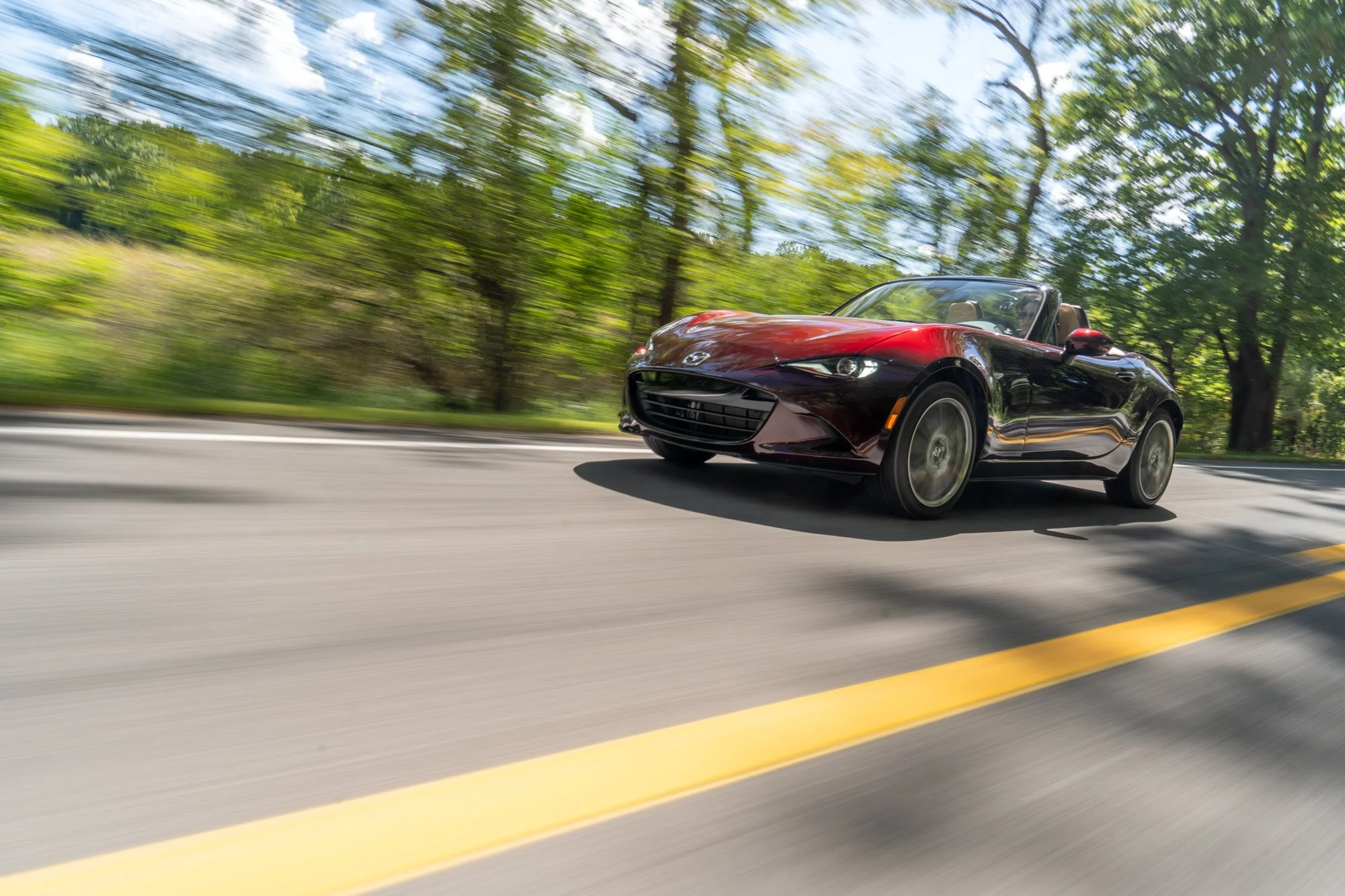 Red convertible sports car driving on a tree-lined road with motion blur.