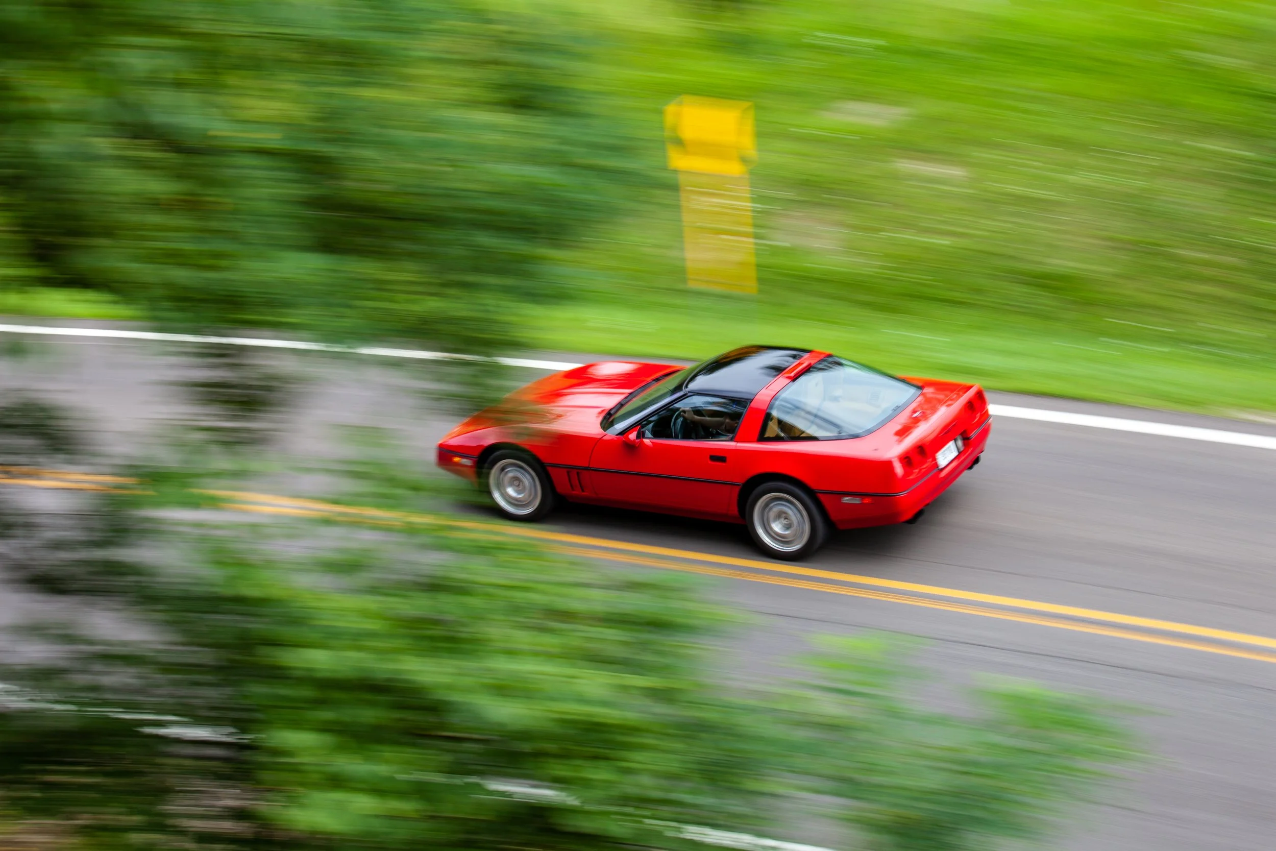 Red sports car driving quickly on a road through a green, forested area.