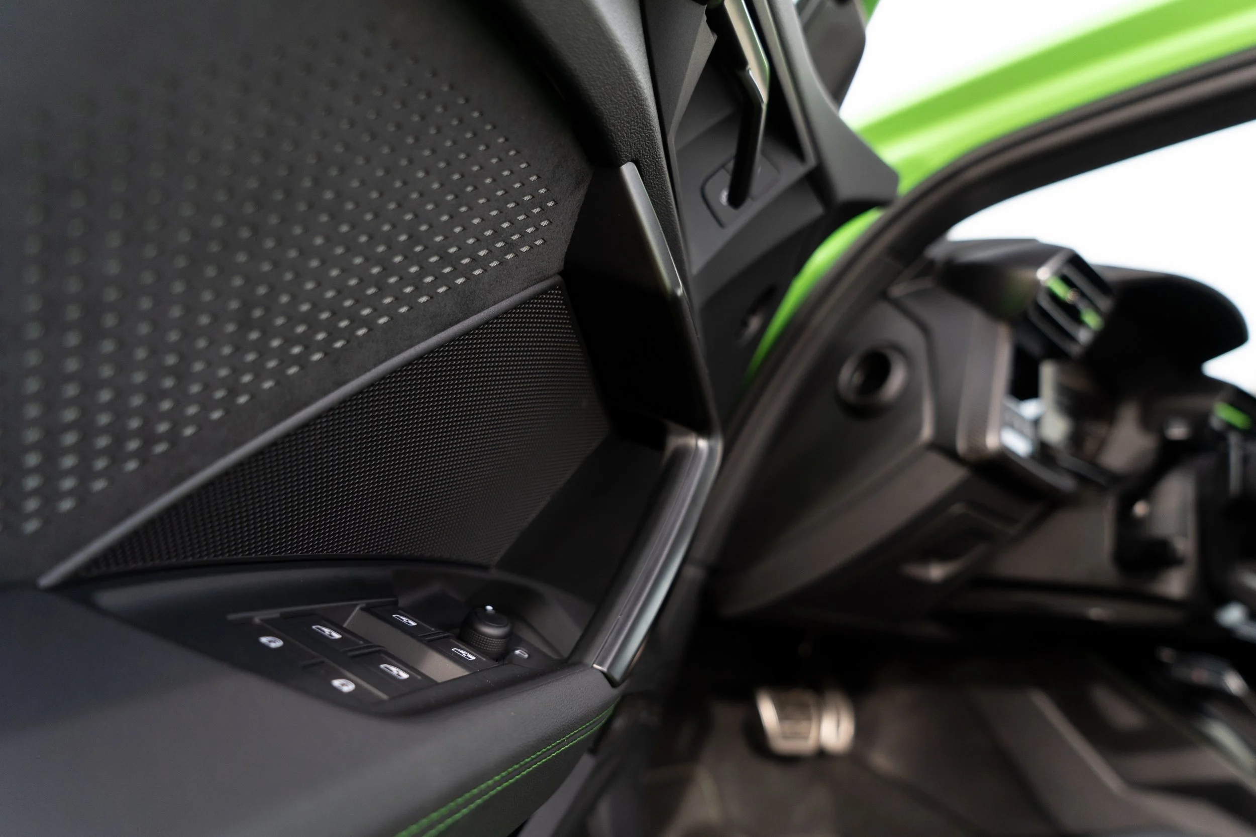 Close-up of the interior of a car, showing the door panel, control buttons, and a speaker grill with a textured surface.