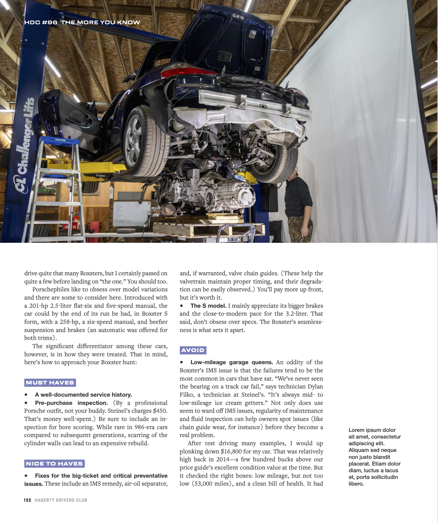 A car mounted on a hydraulic lift in a workshop, with its hood open, exposing the engine. A person is standing underneath the car, inspecting or working on it. The workshop has a wooden ceiling and walls, with tools and equipment in the background. T