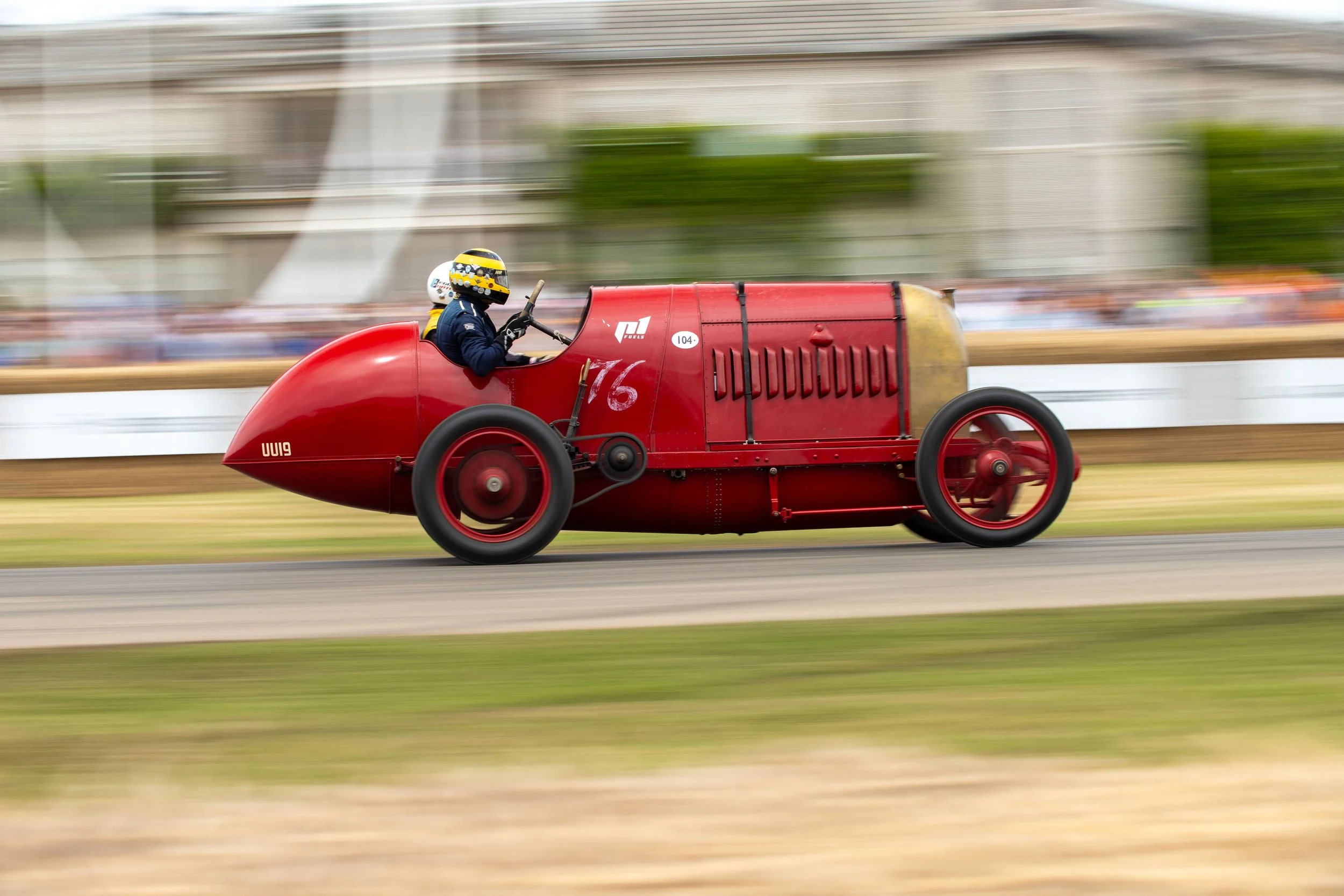 Vintage red racing car speeding along a track with a blurred background.