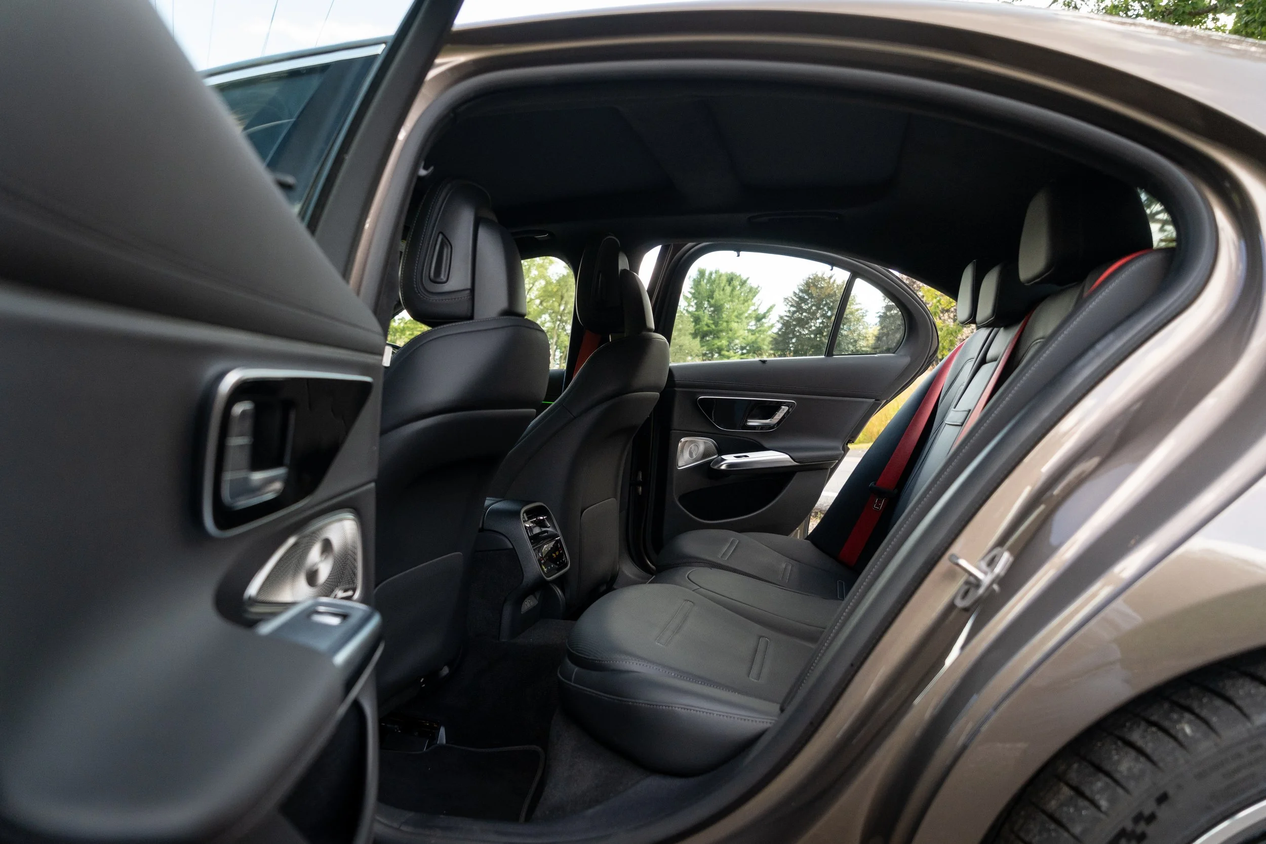 The interior of a modern car showing the back seats, front seats, and door panels with black upholstery and silver accents, with trees visible through the windows.