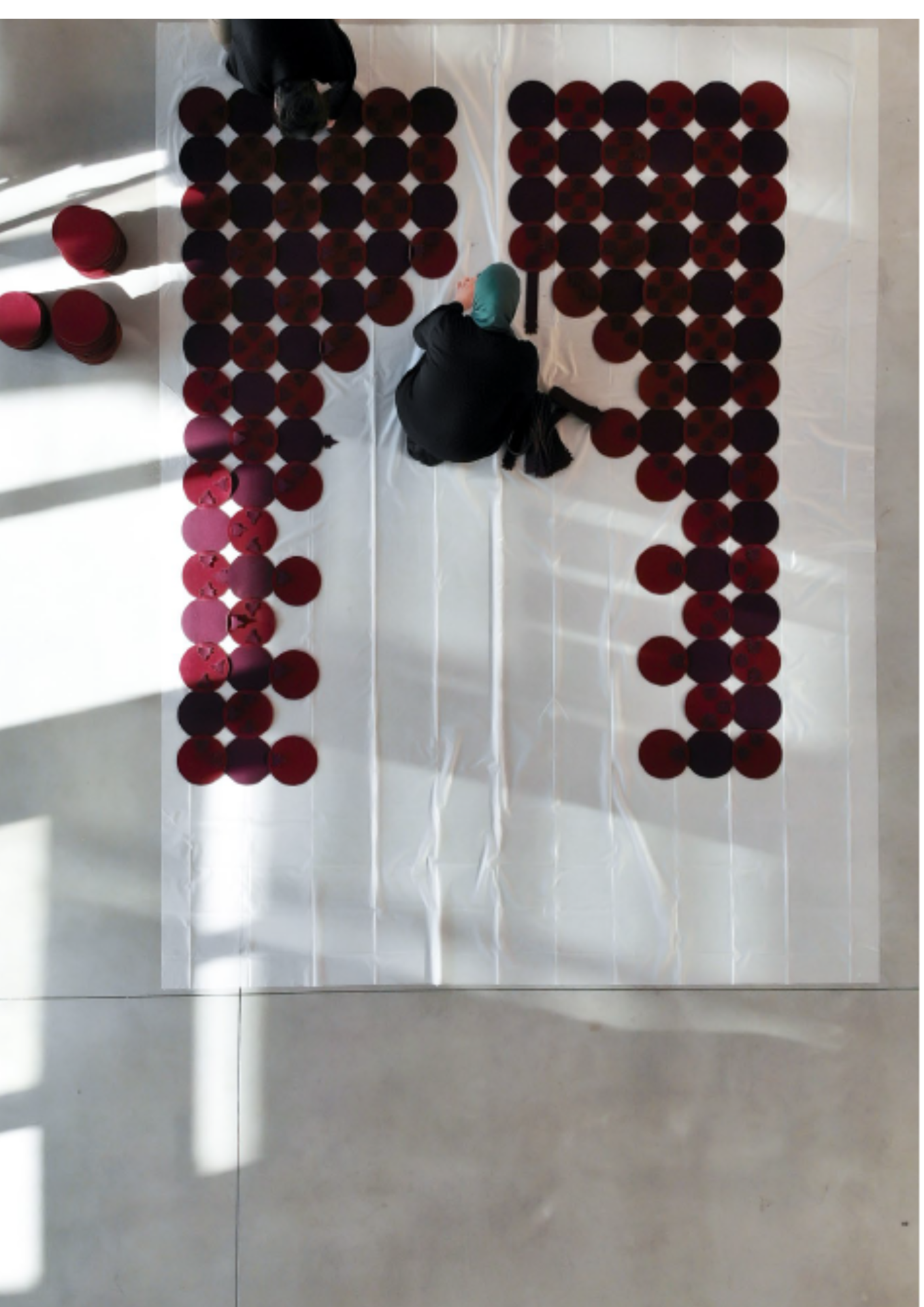 Une personne moyenne s'occupe de disposer des balles rouges et noires en rangées sur un sol blanc, probablement dans un espace intérieur. Il y a des piles de balles empilées à gauche.