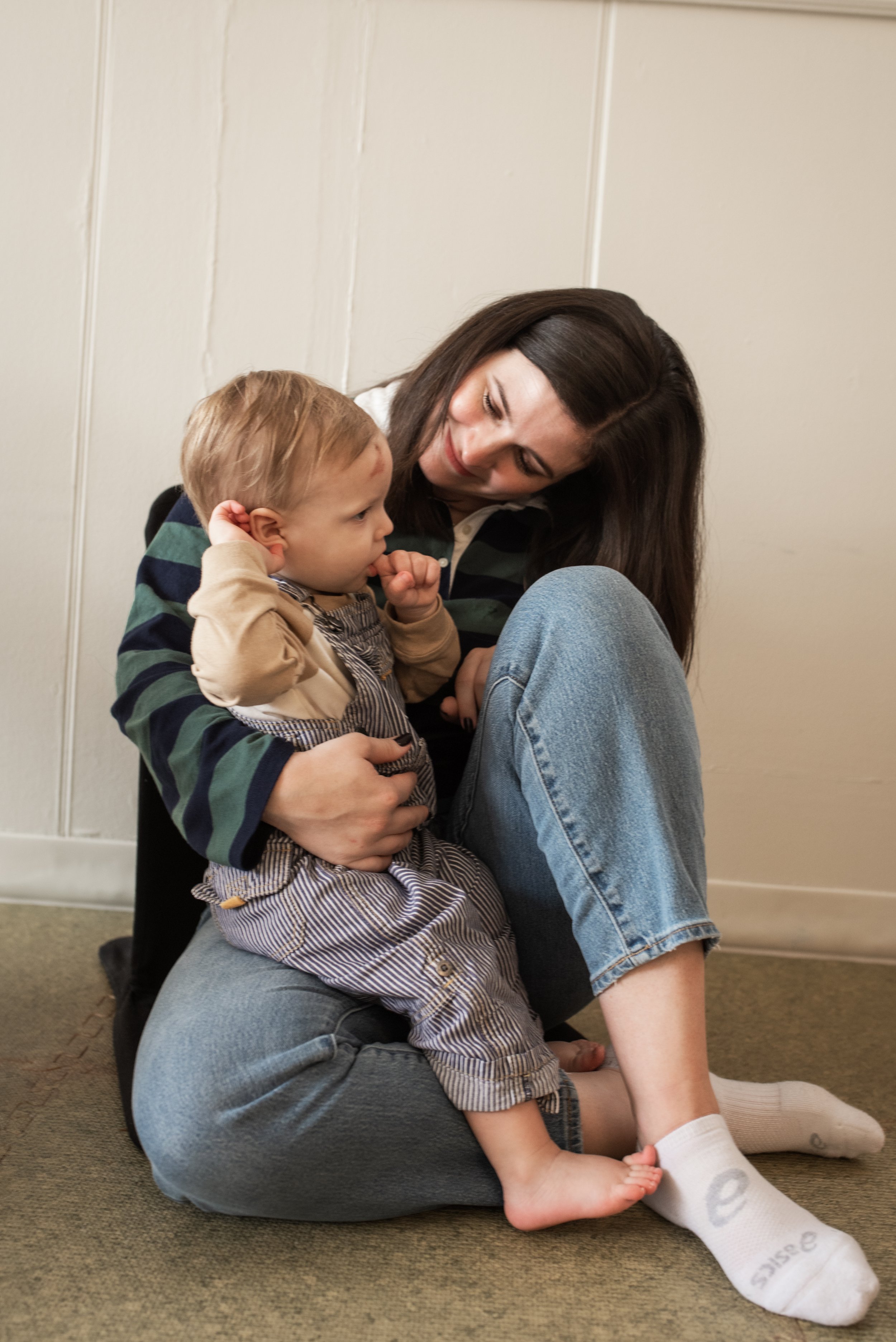A woman sitting on the floor with a child on her lap, both smiling and looking at each other.