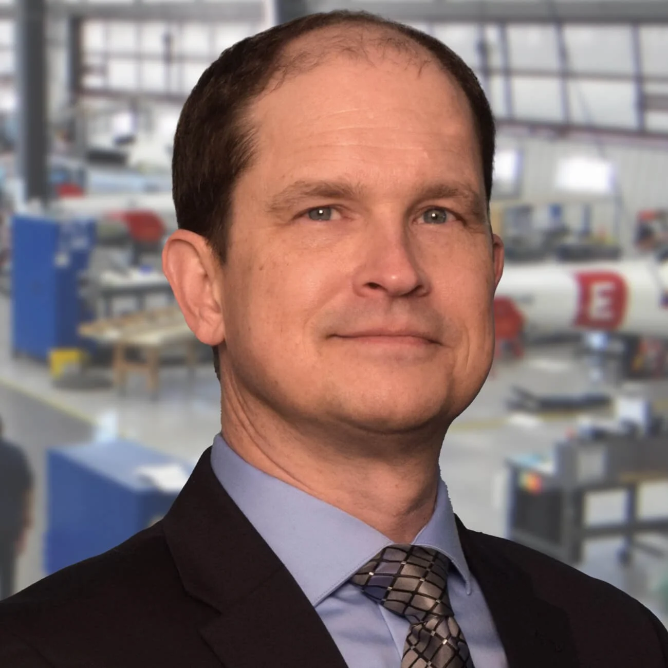 A man in a suit and tie with a blurred industrial background.