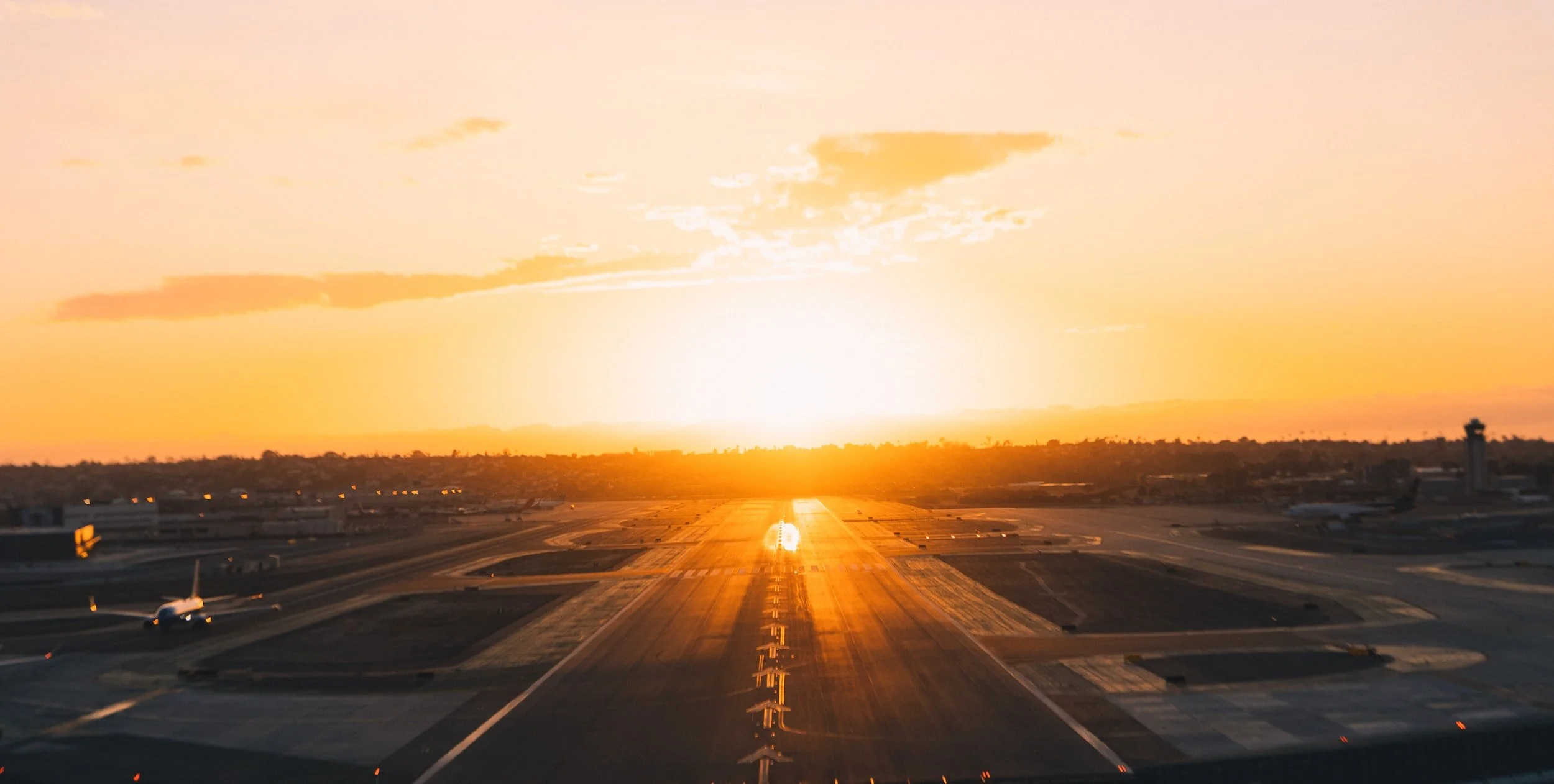 Airport runway at sunset with aircraft taxiing
