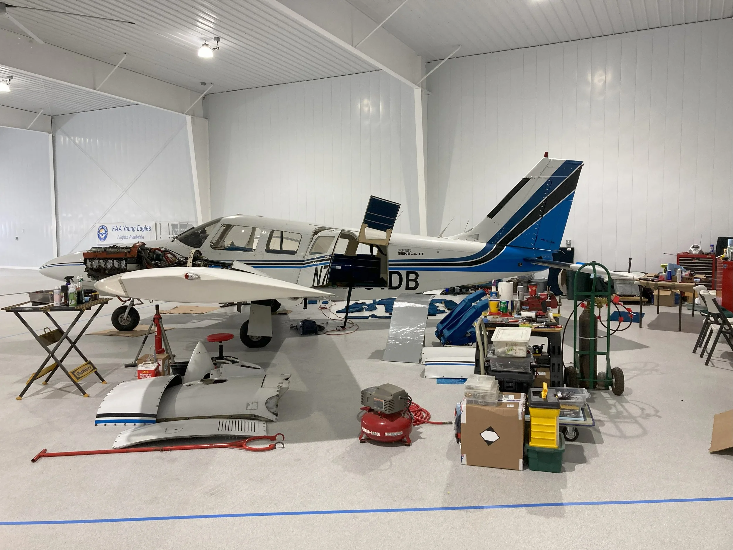 Small aircraft under maintenance in a hangar with various tools and parts scattered around.