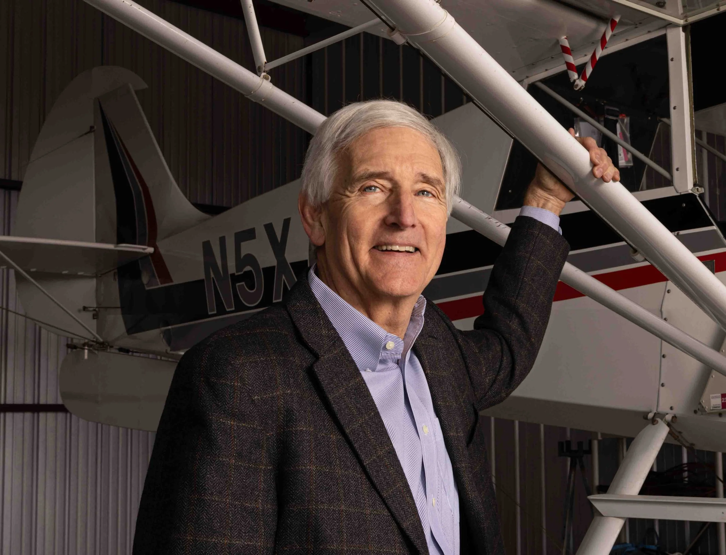 Man in a suit next to a small airplane inside a hangar.