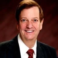 Portrait of a smiling man in a suit against a dark background.