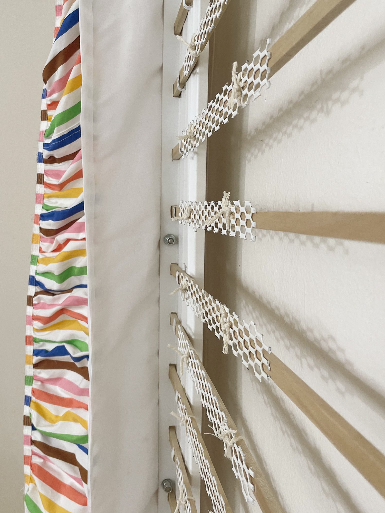 Untitled (Pride Face-hugger), 2025, 78h x 63w x 9d - salvaged wood pallets, poplar wood trim, recycled polyester white backdrop, Target Pride collection 2024 sun dress, Ikea metal white wall shelves and white metal mesh, string, threaded rod, wood gl