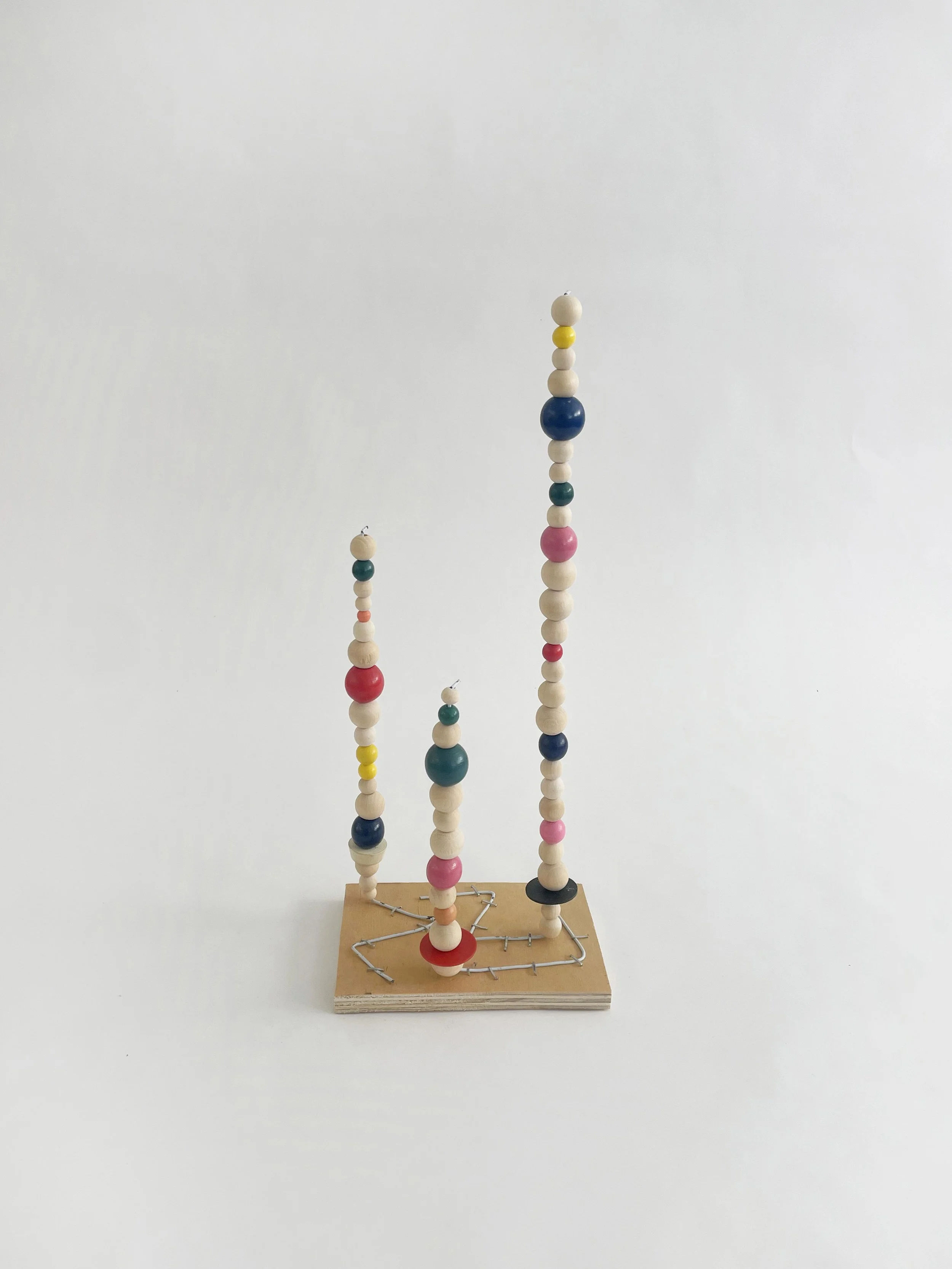 Untitled (watts tower), 2026, 16h x 6w 4d - natural and color wood beads, wire hangers, heavy duty staples, plywood, felt. 