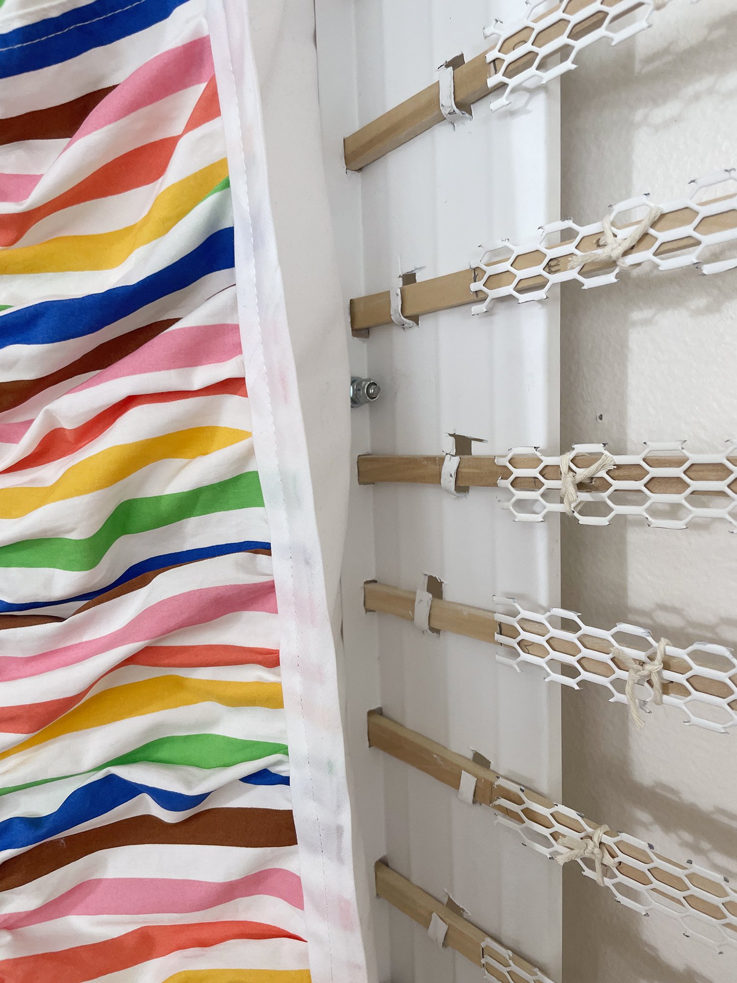 Untitled (Pride Face-hugger), 2025, 78h x 63w x 9d - salvaged wood pallets, poplar wood trim, recycled polyester white backdrop, Target Pride collection 2024 sun dress, Ikea metal white wall shelves and white metal mesh, string, threaded rod, wood gl