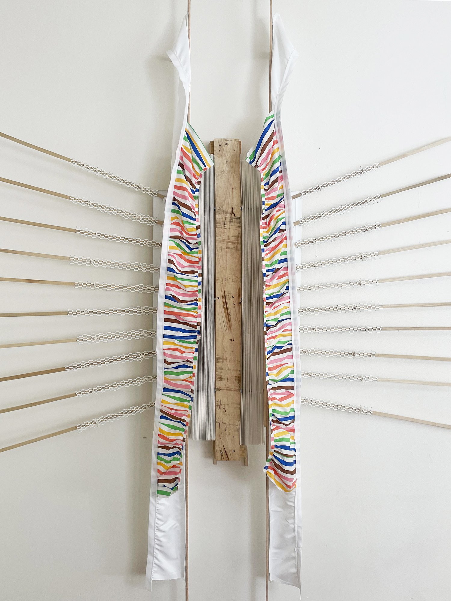 Untitled (Pride Face-hugger), 2025, 78h x 63w x 9d - salvaged wood pallets, poplar wood trim, recycled polyester white backdrop, Target Pride collection 2024 sun dress, Ikea metal white wall shelves and white metal mesh, string, threaded rod, wood gl