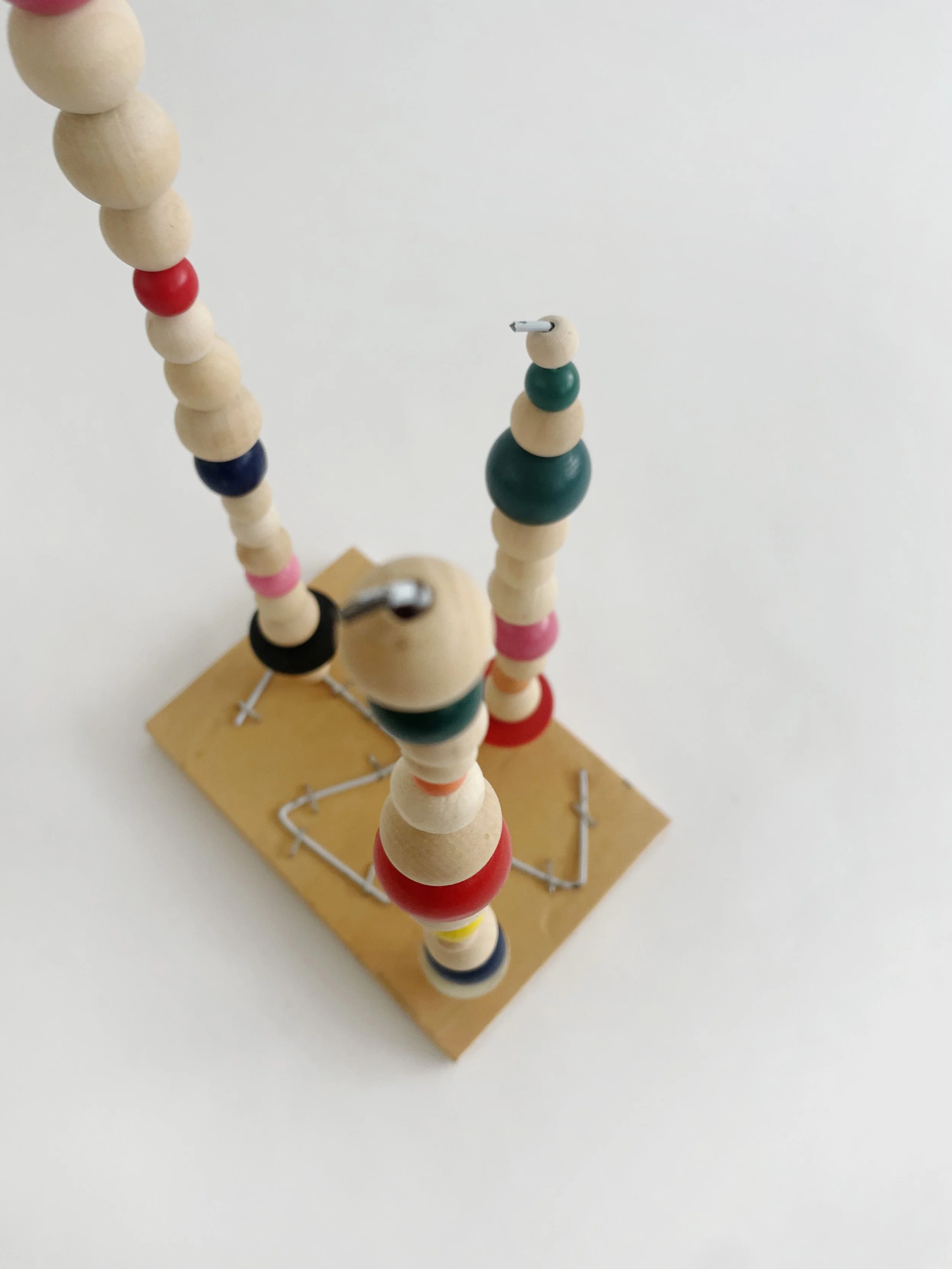 Untitled (watts tower), 2026, 16h x 6w 4d - natural and color wood beads, wire hangers, heavy duty staples, plywood, felt. 