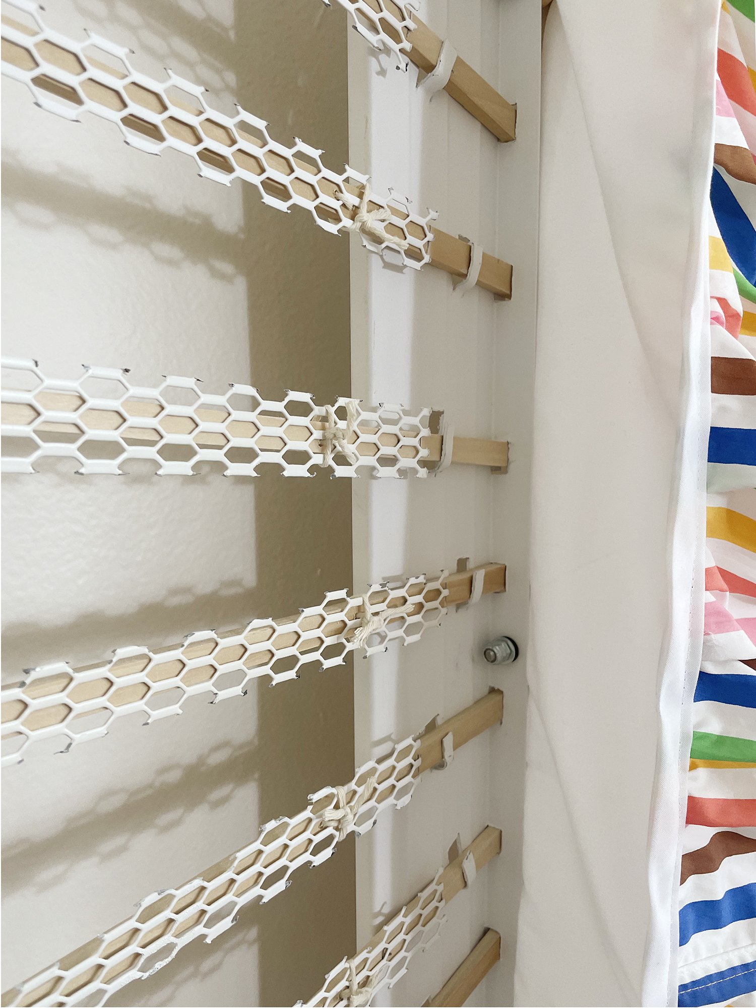 Untitled (Pride Face-hugger), 2025, 78h x 63w x 9d - salvaged wood pallets, poplar wood trim, recycled polyester white backdrop, Target Pride collection 2024 sun dress, Ikea metal white wall shelves and white metal mesh, string, threaded rod, wood gl