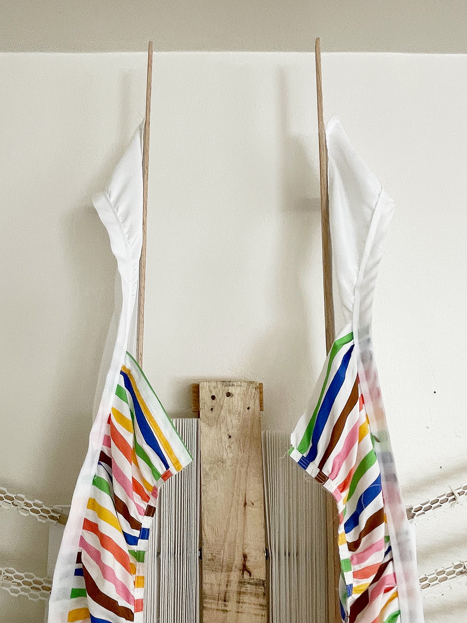 Untitled (Pride Face-hugger), 2025, 78h x 63w x 9d - salvaged wood pallets, poplar wood trim, recycled polyester white backdrop, Target Pride collection 2024 sun dress, Ikea metal white wall shelves and white metal mesh, string, threaded rod, wood gl